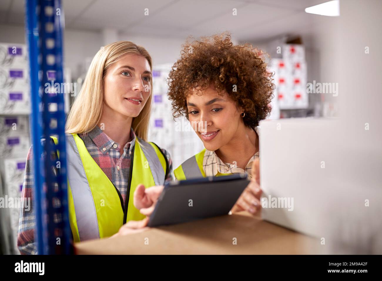 Two Female Workers In Logistics Distribution Warehouse Using Digital Tablet Stock Photo