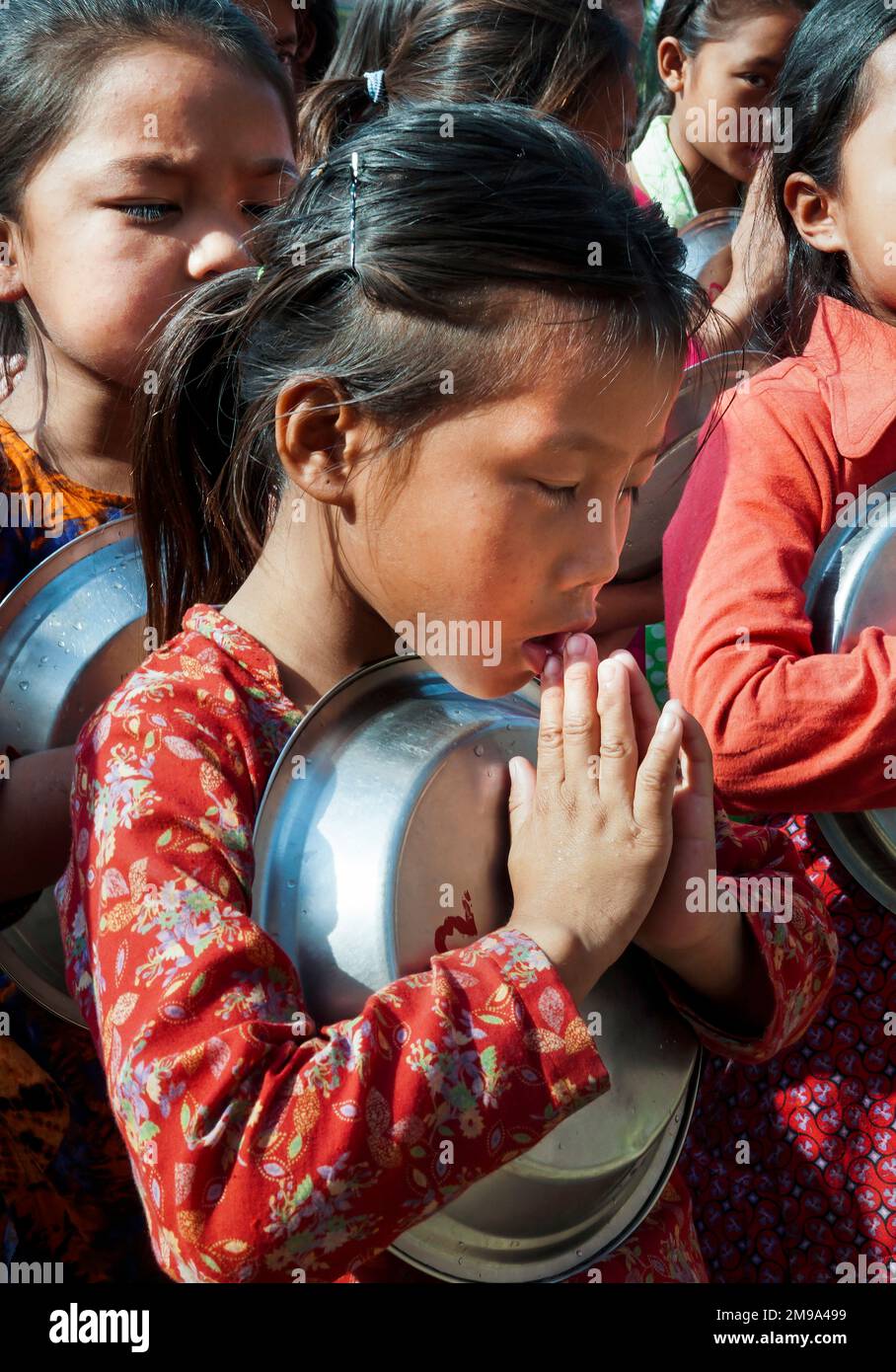 Schülerinnen der Novodaya-Chepang-Schule in Chitwan, Nepal beten vor dem Essen mit ihren noch leeren Tellern in der Hand Stock Photo