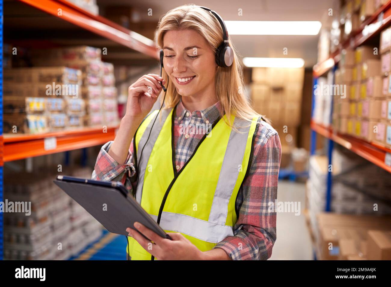 Female Worker Wearing Headset In Logistics Distribution Warehouse Using Digital Tablet Stock Photo