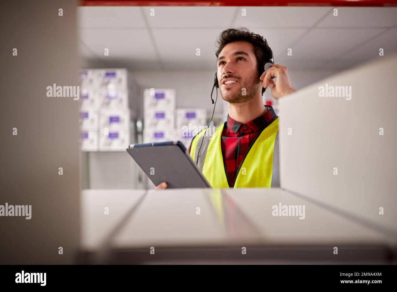 Male Worker Wearing Headset In Logistics Distribution Warehouse Using Digital Tablet Stock Photo