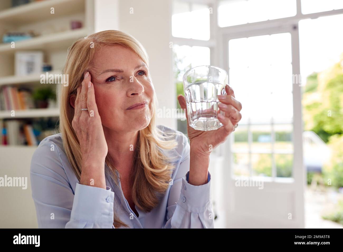 Menopausal Mature Woman At Home Suffering With Headache Pain Drinking