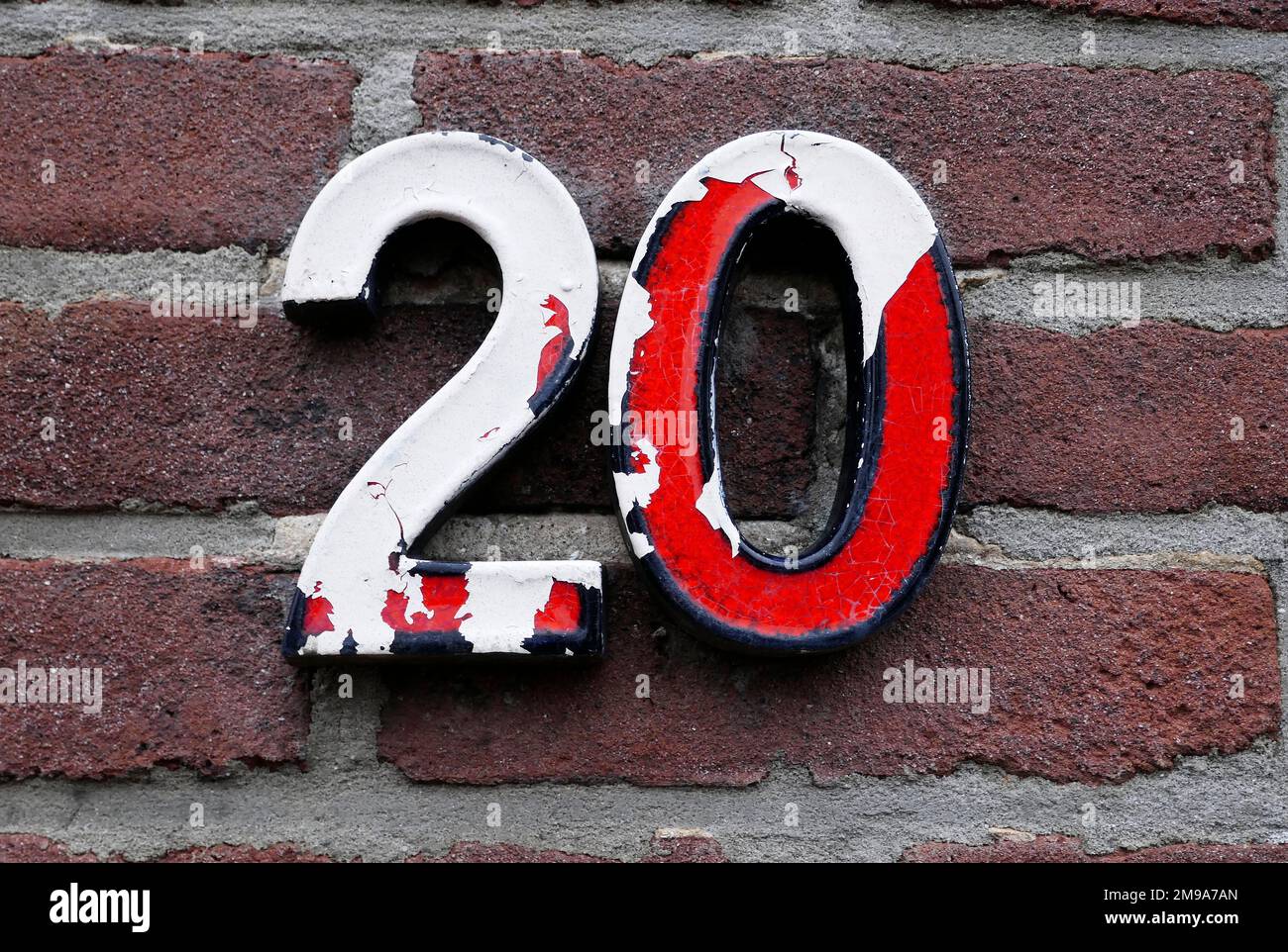 Number 20 in red  numbers on a brick wall. Half of the red paint is gone. The white is left. These kinds of house numbers were fashionable in the Neth Stock Photo