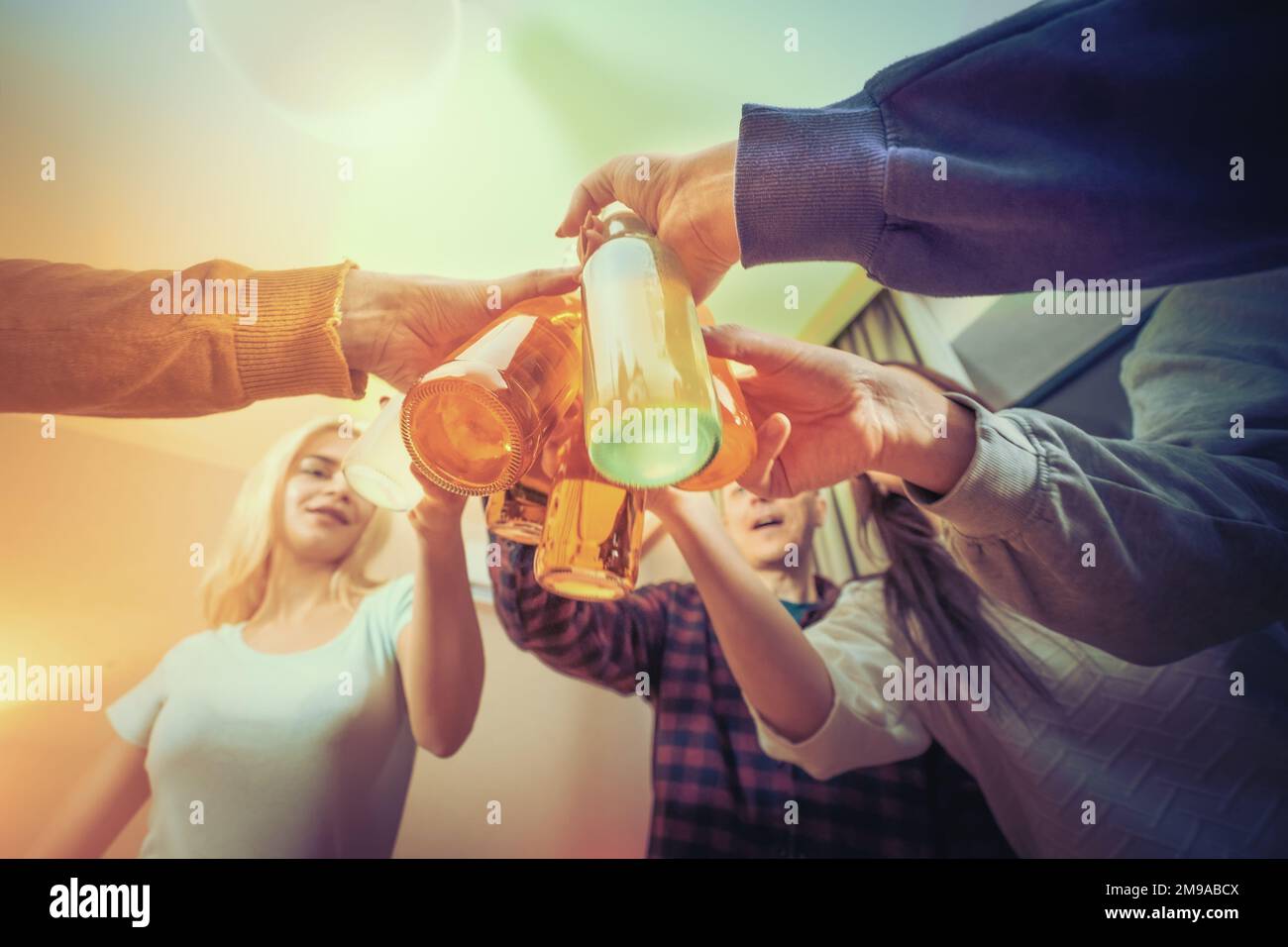 Friends clinking bottles of beer at home party, close up on hands. Celebration and holidays concept. Stock Photo