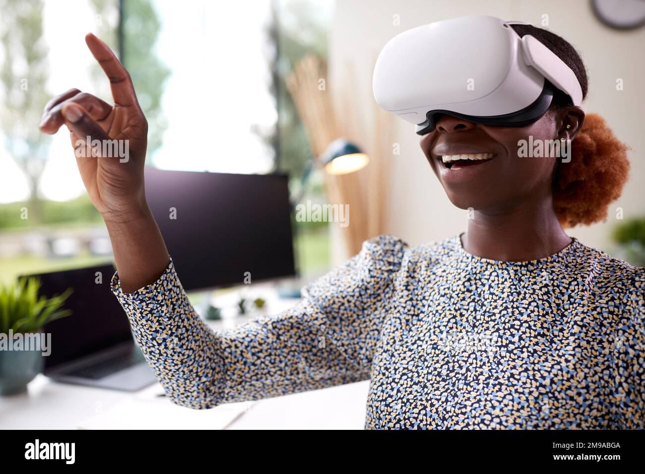 Woman Working From Home Office Sitting At Desk Wearing VR Headset Interacting With AR Technology Stock Photo