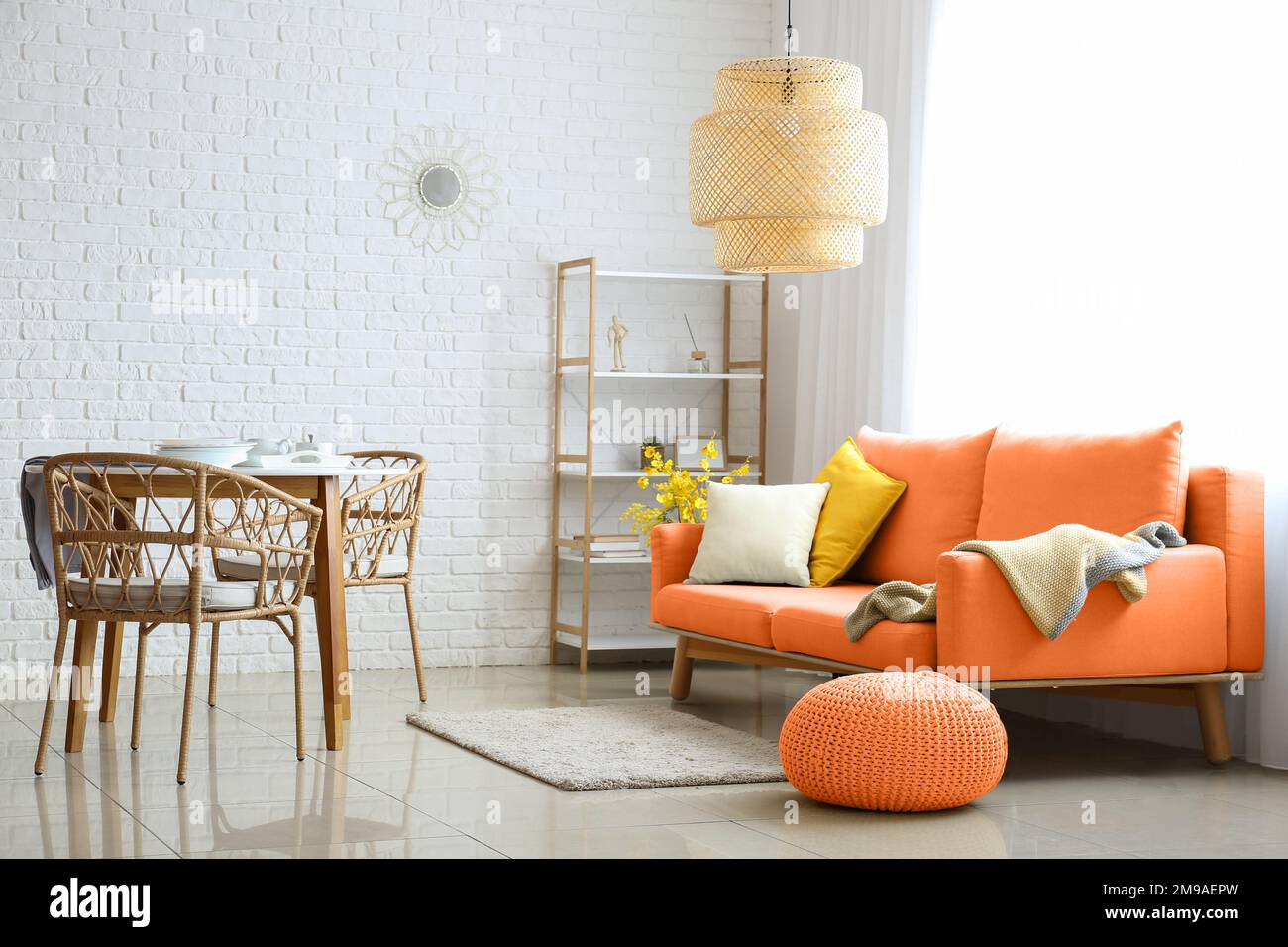 Stylish interior of living room with orange sofa, pouf and dining table ...