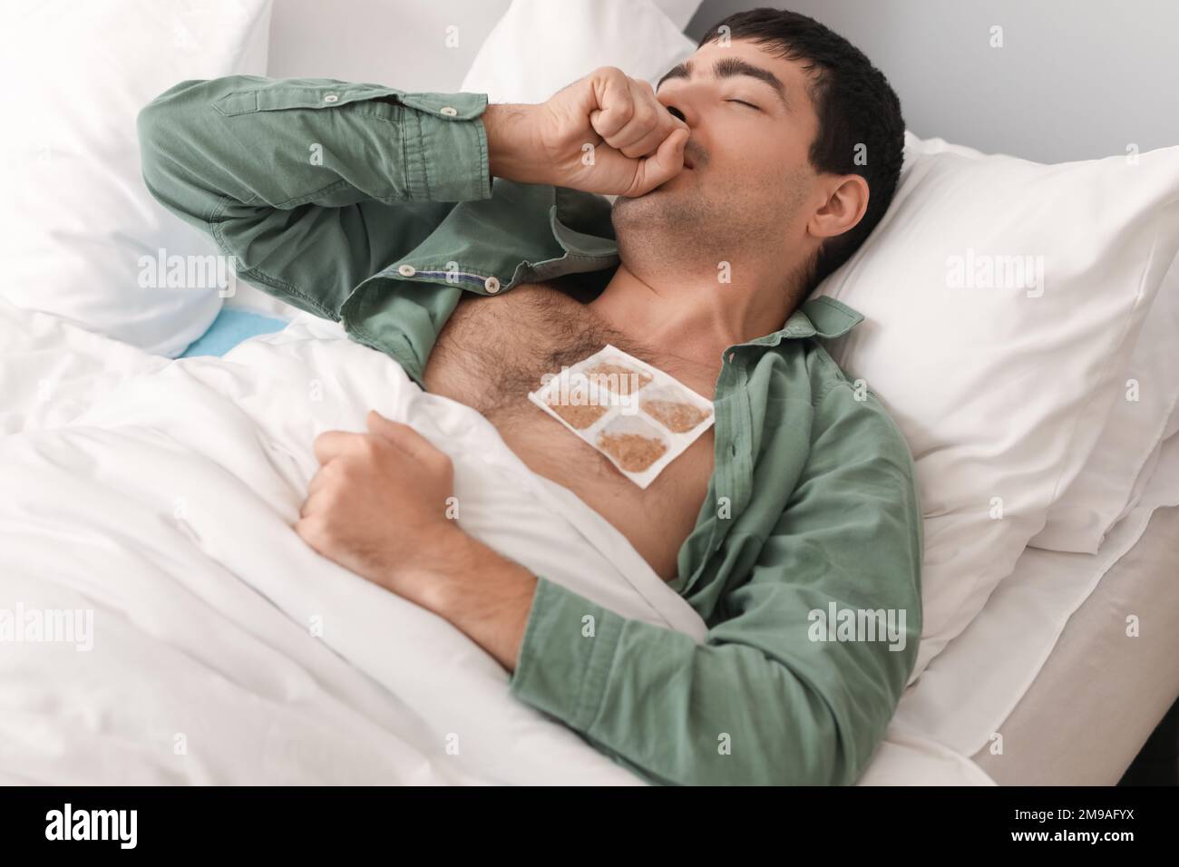 Ill young man with mustard plaster on his chest lying in bedroom Stock