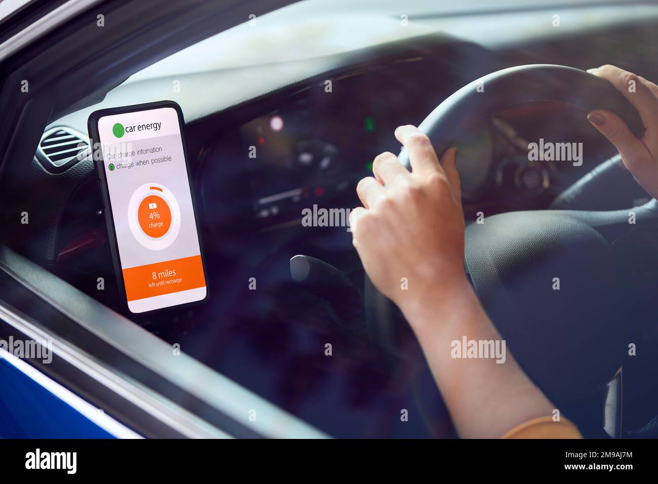 Woman Driving Electric Car With Cable Using App On Phone To Monitor