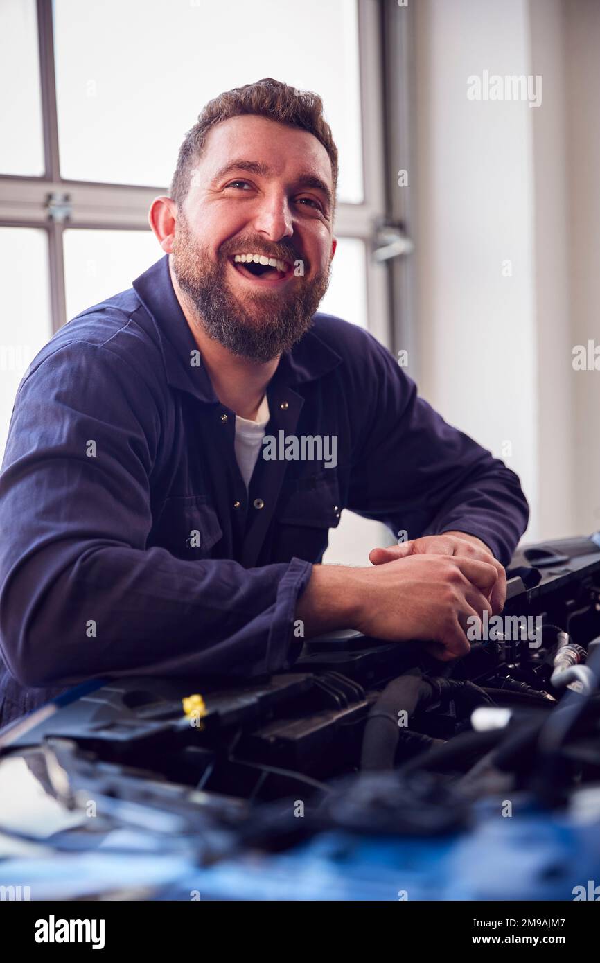 Male Mechanic In Garage Looking Under Hood Of Car Whilst Servicing Engine Stock Photo