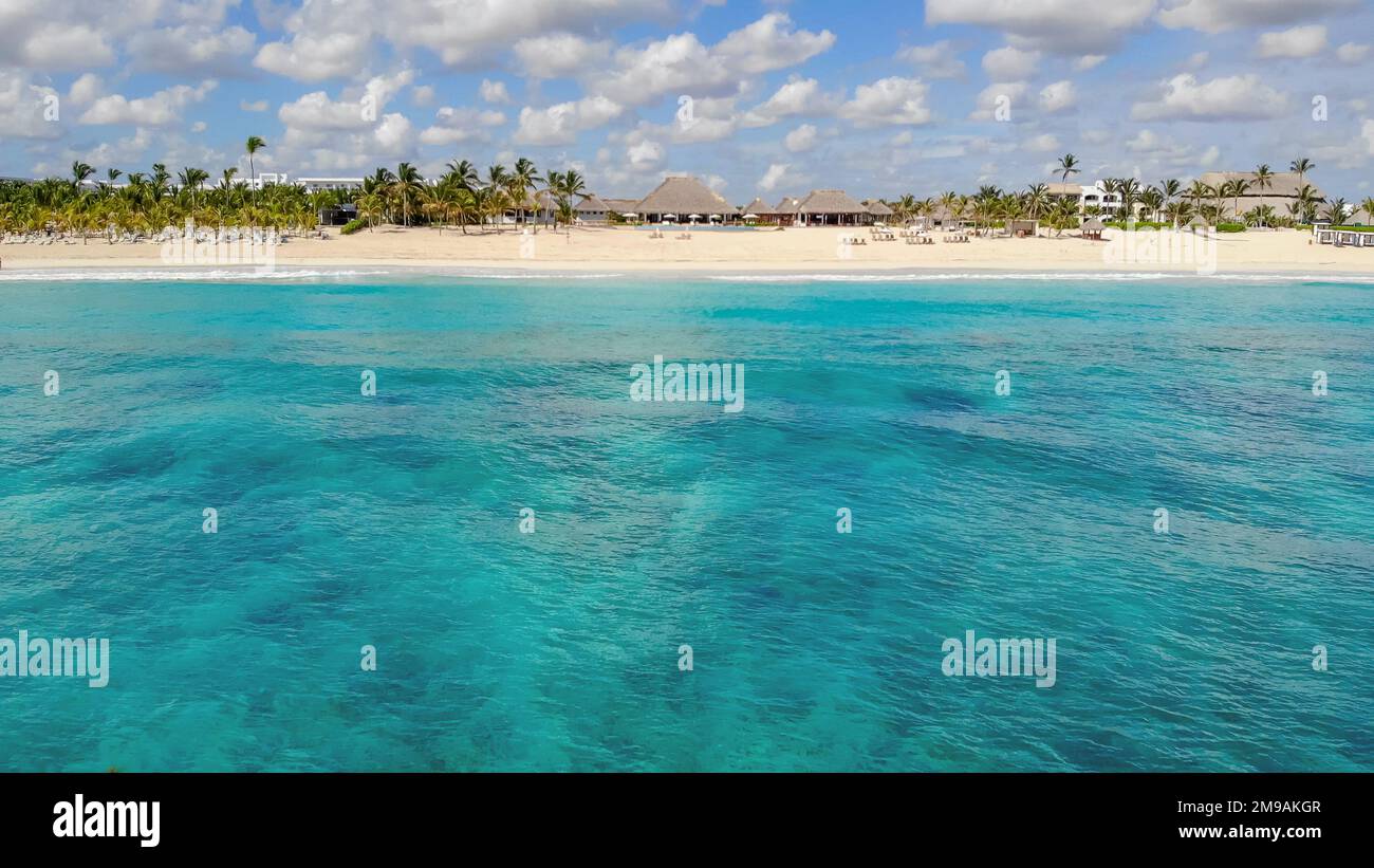 Drone view ander azure clear sea water. Aerial View To Thatched Rooftop Building Surrounded By Palm Trees And Resort Buildings On Caribbean Beach. Aerial view of resort Punta Cana Stock Photo
