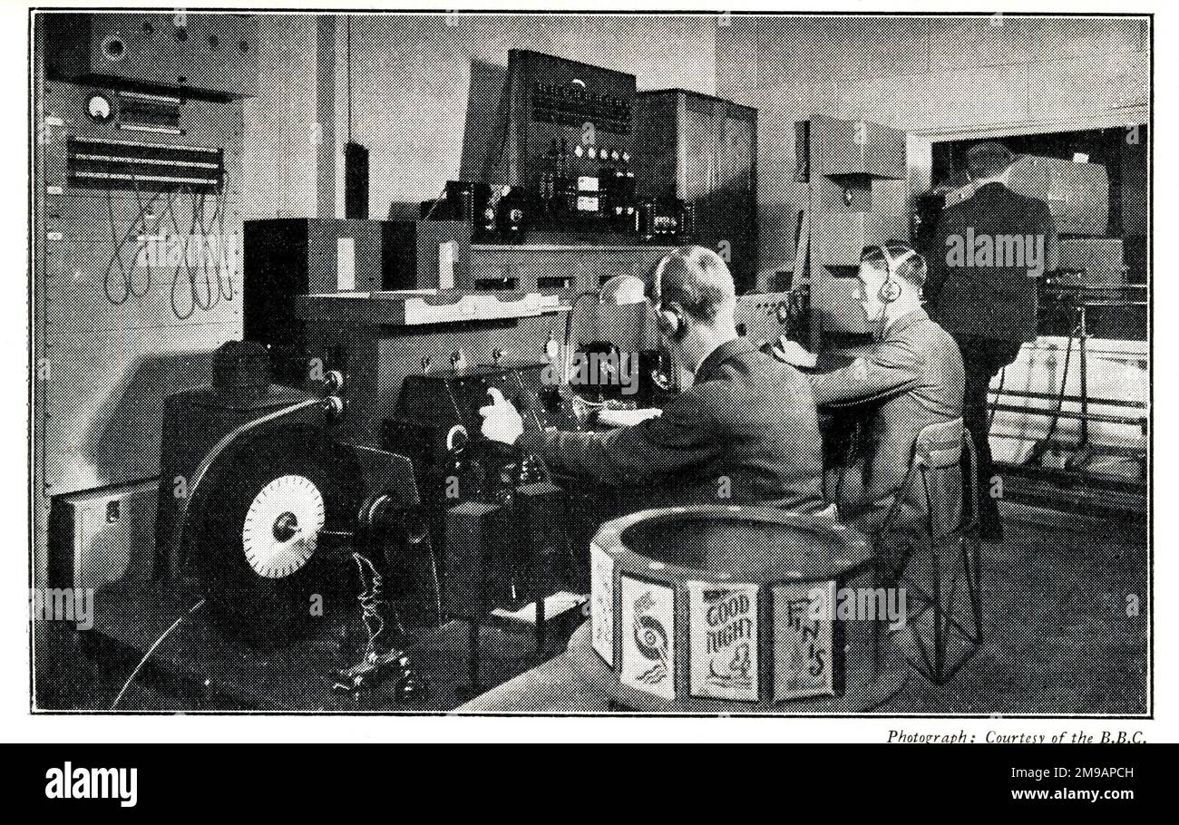 BBC Late Low Definition Television Control Room. On the right is the mirror-drum projection scanner, on the left are the two checking receivers. The engineers in position (R to L) are projectionist, vision-control, sound and caption control. The BBC 'tuning in' design can be seen in the transmitter (caption) drum in the foreground. Stock Photo
