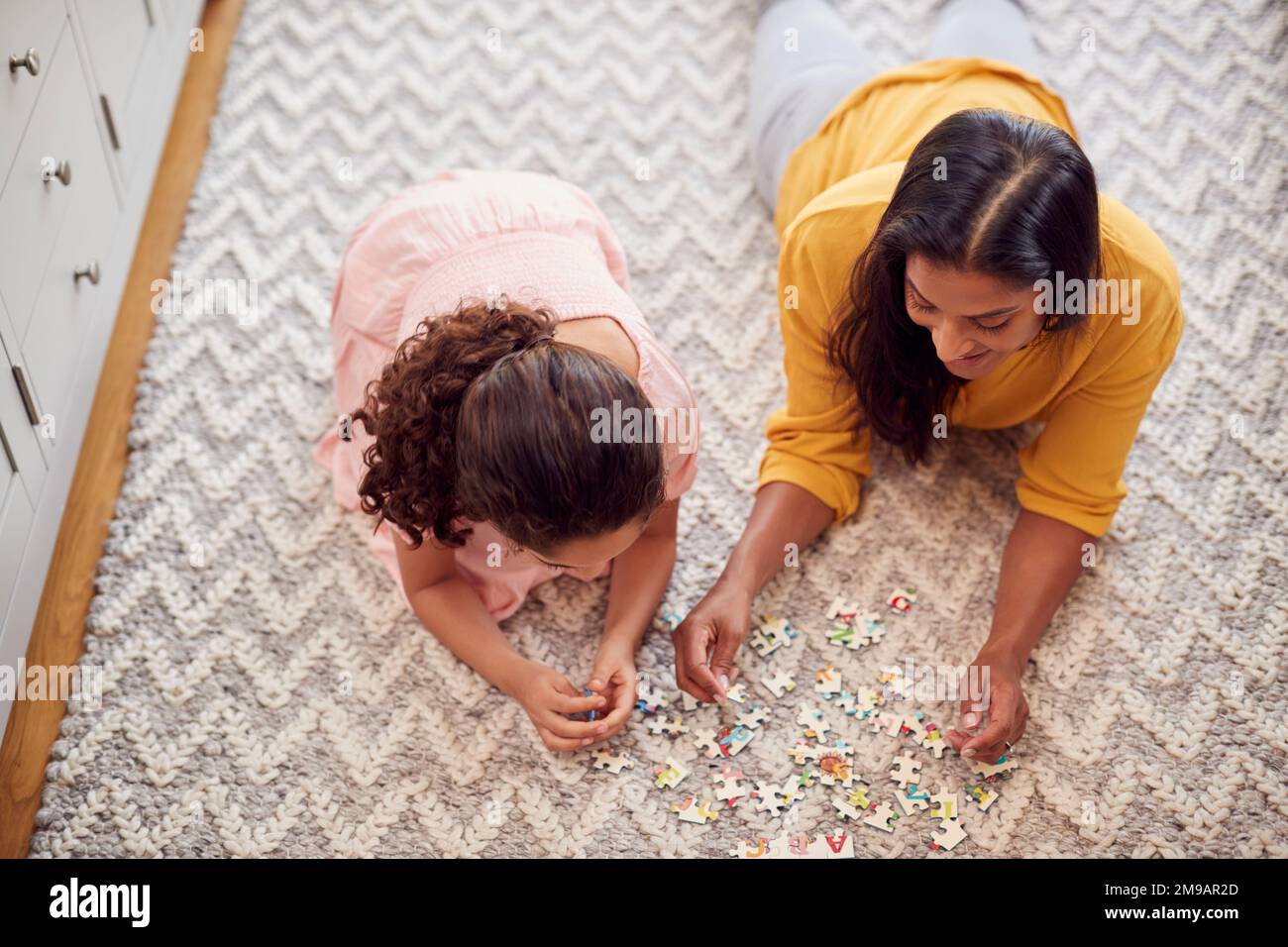 Mother And Daughter At Home Lying On Floor In Lounge Doing Jigsaw