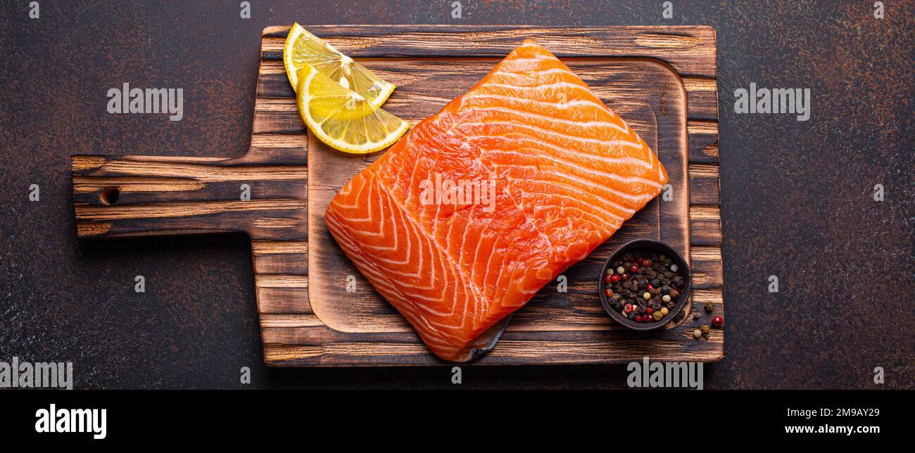 Fresh raw salmon fillet on wooden kitchen cutting board with seasonings ...