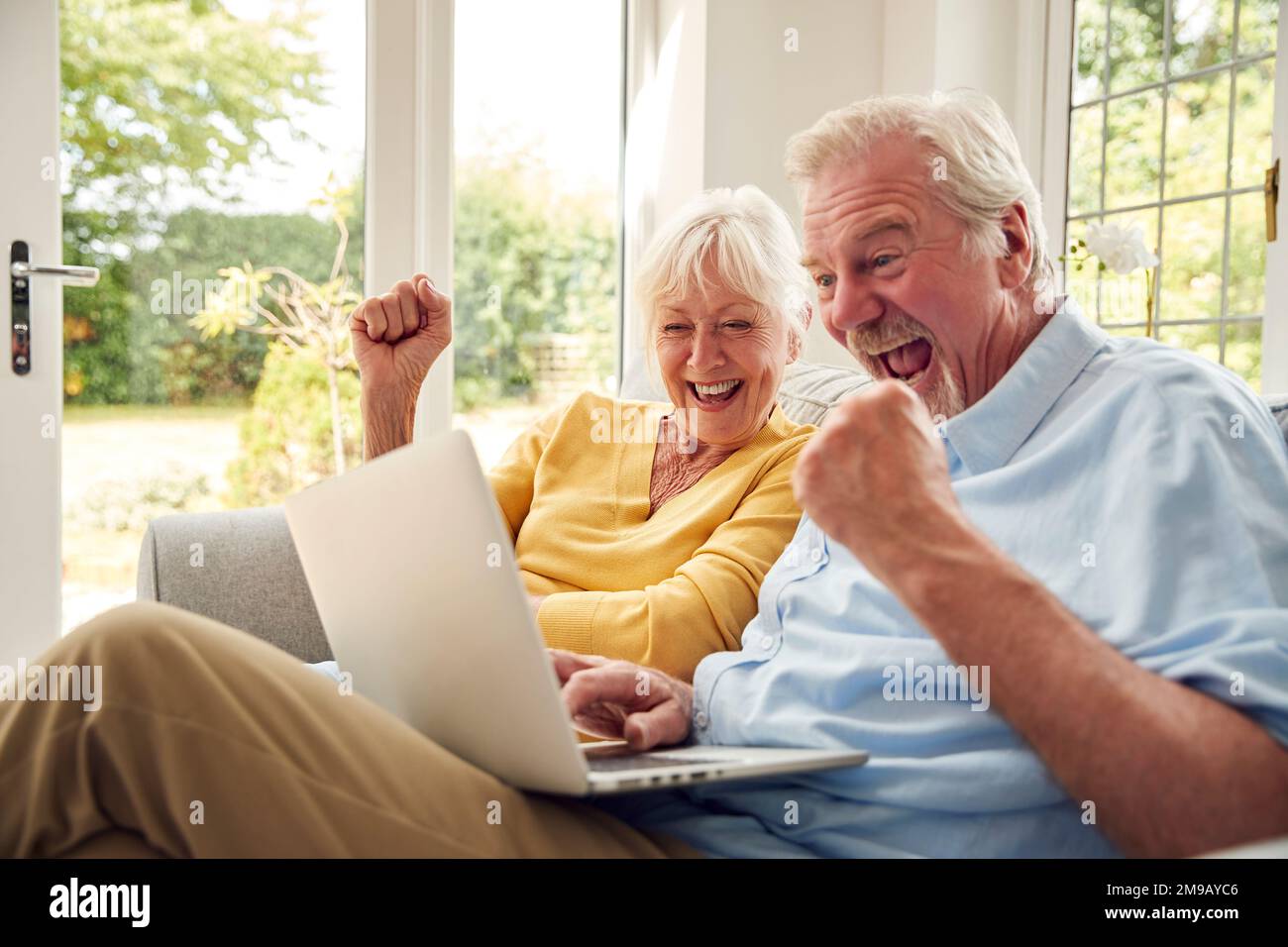 Retired Senior Couple Sitting On Sofa At Home Using Laptop Stock Photo
