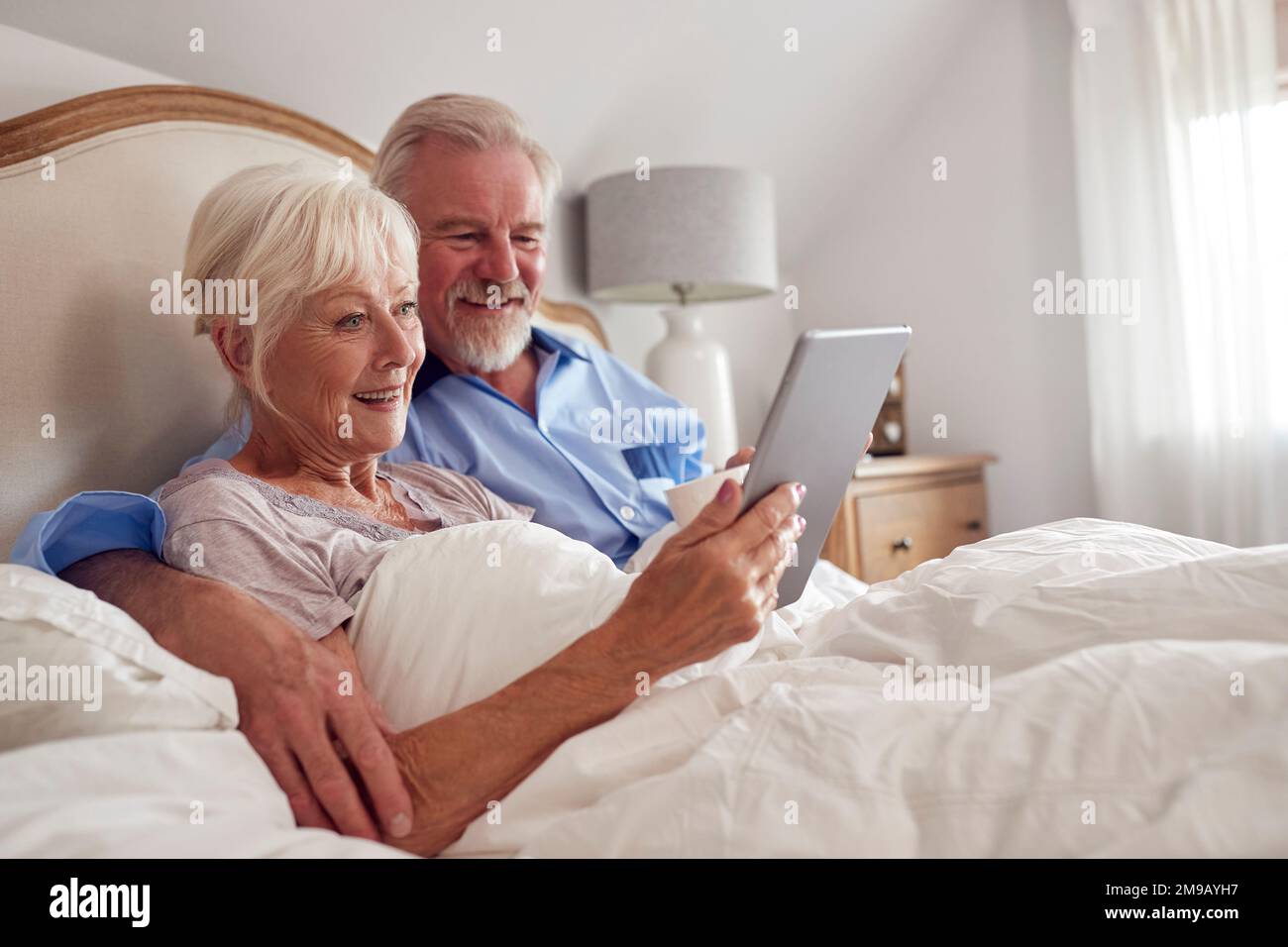 Retired Senior Couple In Bed At Home Using Digital Tablet Stock Photo