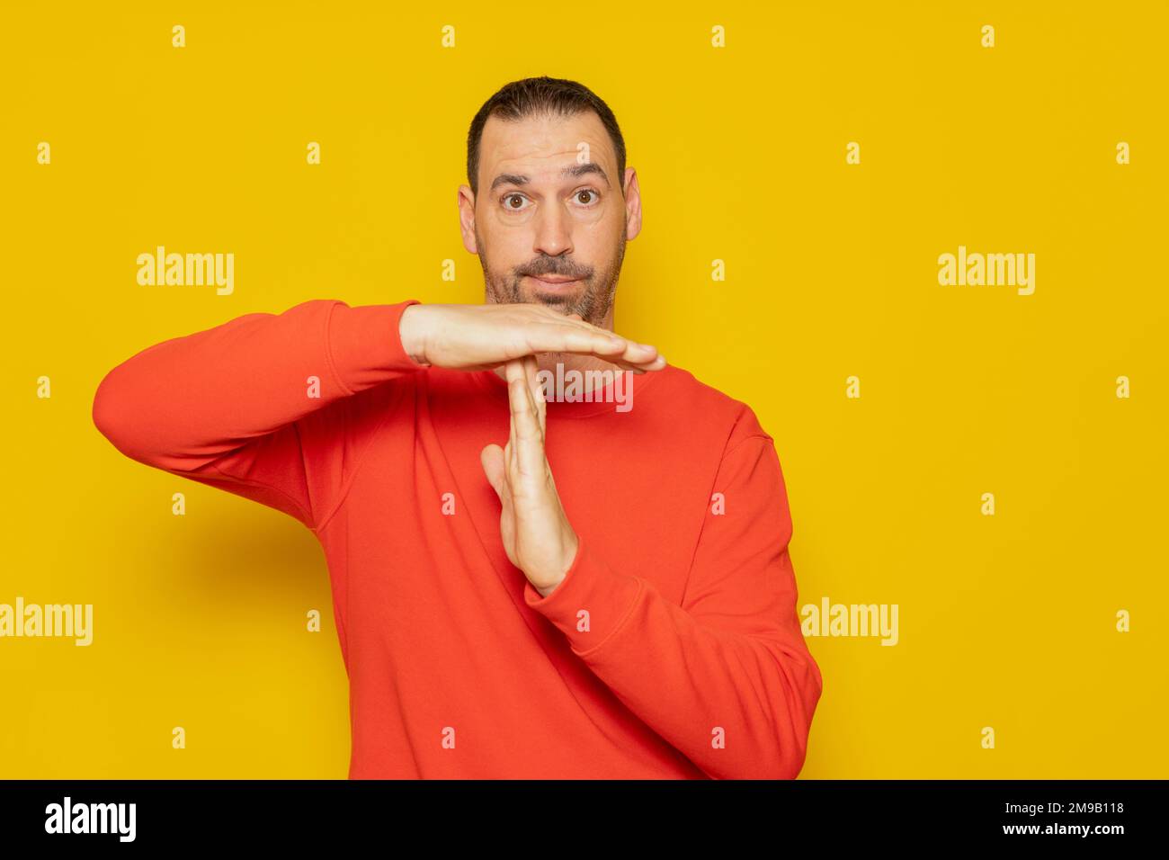 Latino man with a beard in a red sweatshirt making the time-out gesture, he needs a break from the pace of life demanded of middle-class people Stock Photo