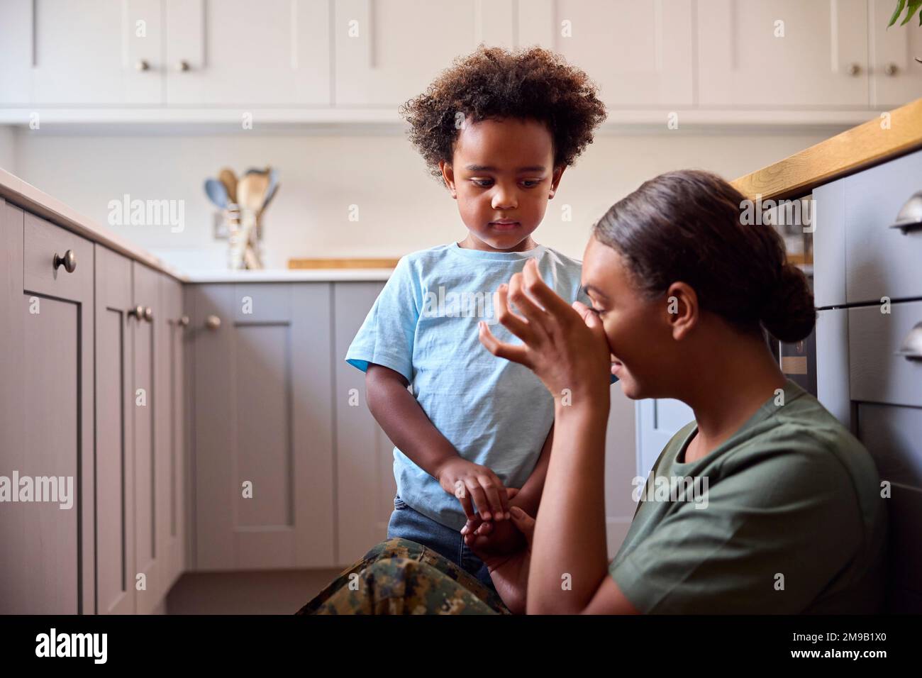 Young Son Comforting Depressed Mother In Uniform Suffering With PTSD Sitting On Floor On Home Leave Stock Photo