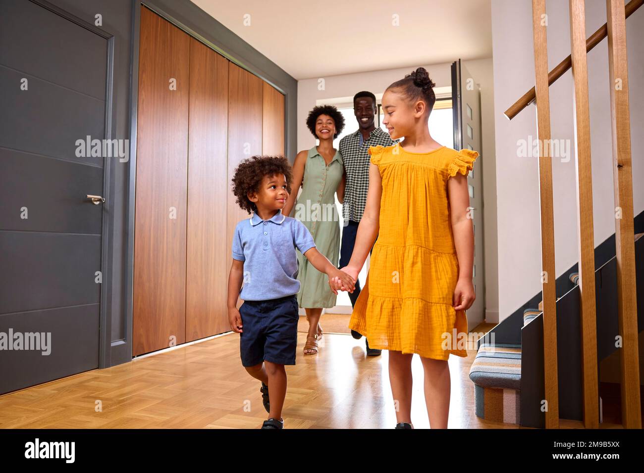 Family Coming Home After Day Out Opening Front Door And Walking Into Hallway Stock Photo