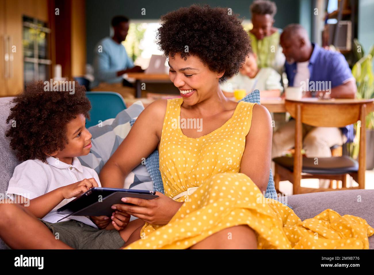 Multi-Generation Family With Mother And Son At Home Using Digital Tablet With Grandparents Behind Stock Photo