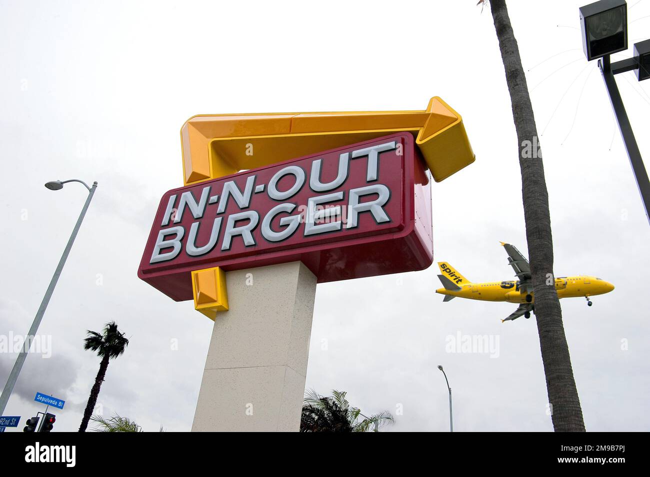 A yellow Spirit Airlines plane is about to land at LAX airport just next to an In-N-Out Burger fast food restaurant in Los Angeles, CA Stock Photo