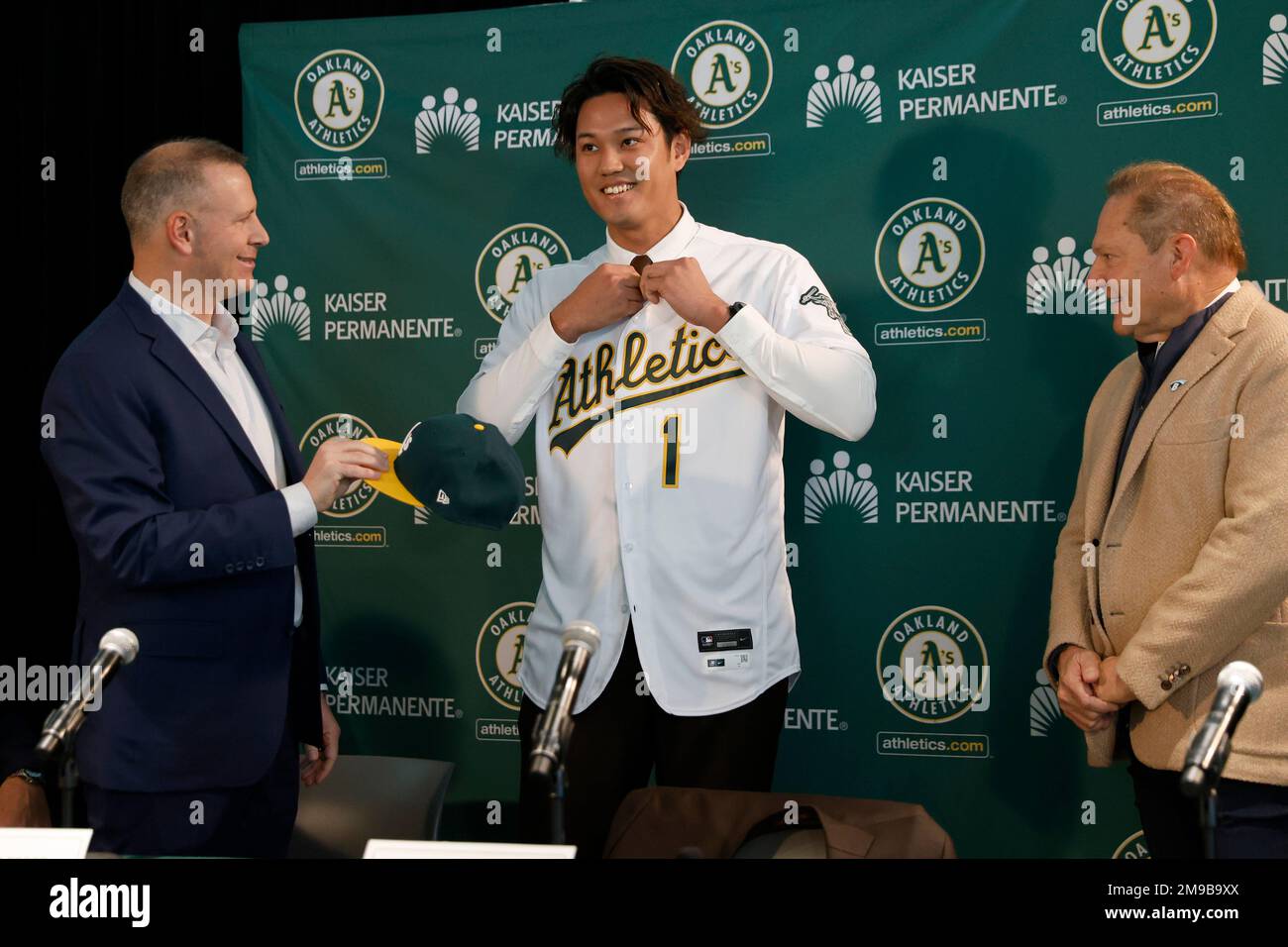 Oakland Athletics pitcher Shintaro Fujinami, center, puts on a jersey with  Athletics' general manager David Forst, left, and agent Scott Boras, right,  during an introductory baseball news conference in Oakland, Calif., Tuesday,