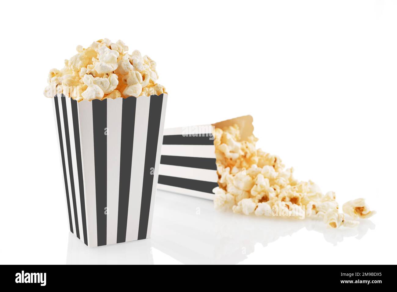 Two black white striped carton buckets with tasty cheese popcorn, isolated on white background. Box with scattering of popcorn grains. Movies, cinema Stock Photo