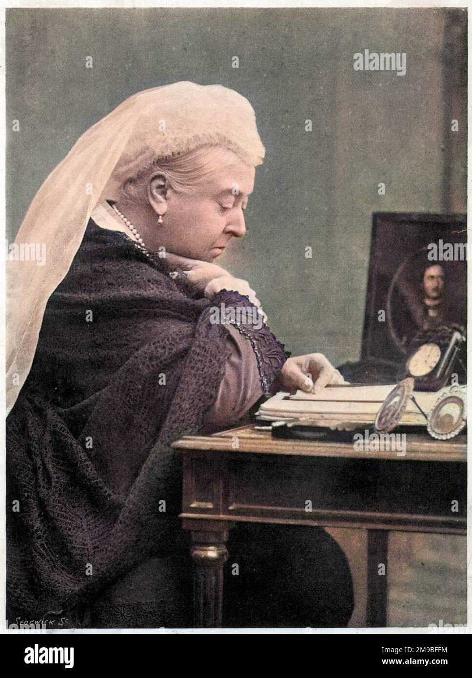 Queen Victoria (1819 - 1901), seated at her desk in the 1890s, with a picture of her deceased husband Prince Albert by her side. Stock Photo