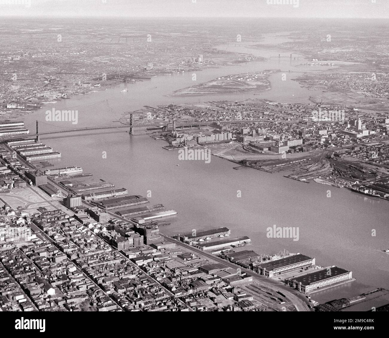 1950s 1960s AERIAL LOOKING NORTH UP DELAWARE RIVER PAST BEN FRANKLIN BRIDGE AND WATERFRONT WHARFS IN PHILADELPHIA PA USA - a1197 HAR001 HARS BOUNDARY DELAWARE RIVER WATERFRONT BLACK AND WHITE HAR001 OLD FASHIONED Stock Photo