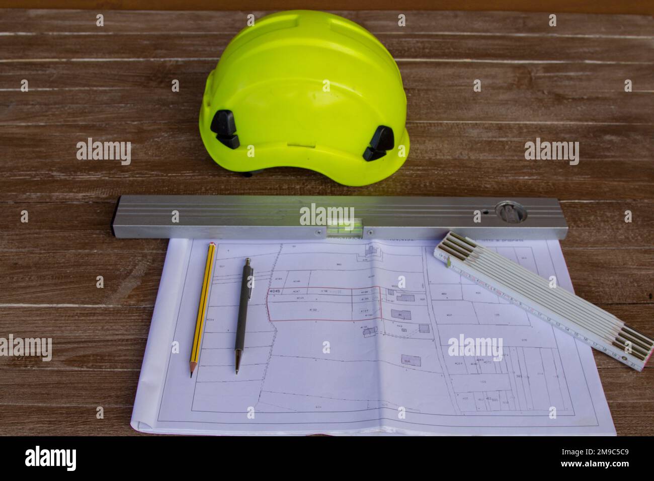 Image of a work table where plans for a building site are placed, a work helmet, a level, tape measure and pencils. Construction engineer job Stock Photo