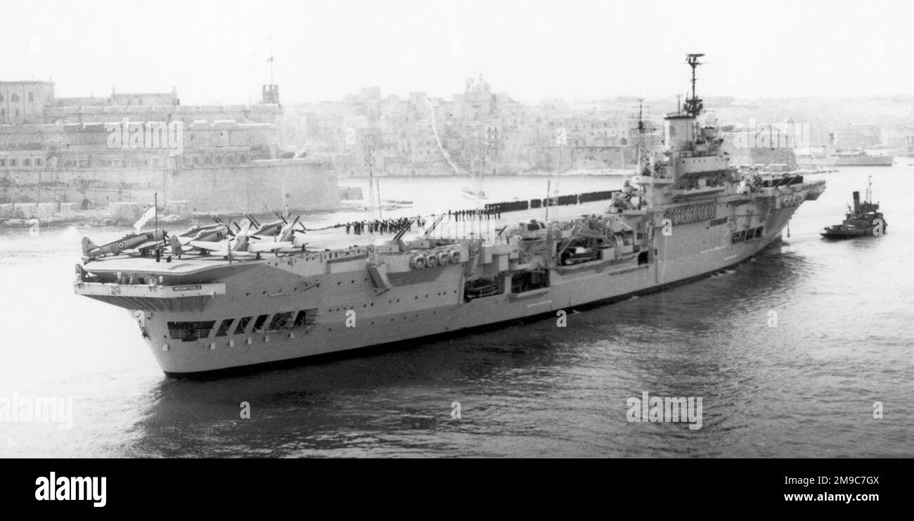 Royal Navy - HMS Indomitable 92, a modified Illustrious-class aircraft carrier, being towed into Valletta harbour in March 1952. Stock Photo