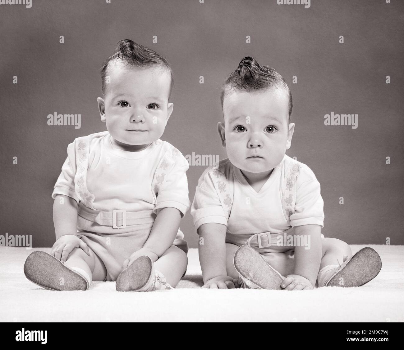 1950s TWIN BABY BOYS 9 MONTHS OLD LOOKING AT CAMERA - b5387 HAR001 HARS FULL-LENGTH MATCH MALES OPPOSITE ENTERTAINMENT EXPRESSIONS B&W MATCHING SAME HUMOROUS HAPPINESS COMICAL SIBLING BABY BOY LOOK-ALIKE COOPERATION DUPLICATE GROWTH JUVENILES LOOK ALIKE MONTHS TOGETHERNESS BIGGER BLACK AND WHITE CAUCASIAN ETHNICITY CLONE HAR001 OLD FASHIONED SMALLER Stock Photo