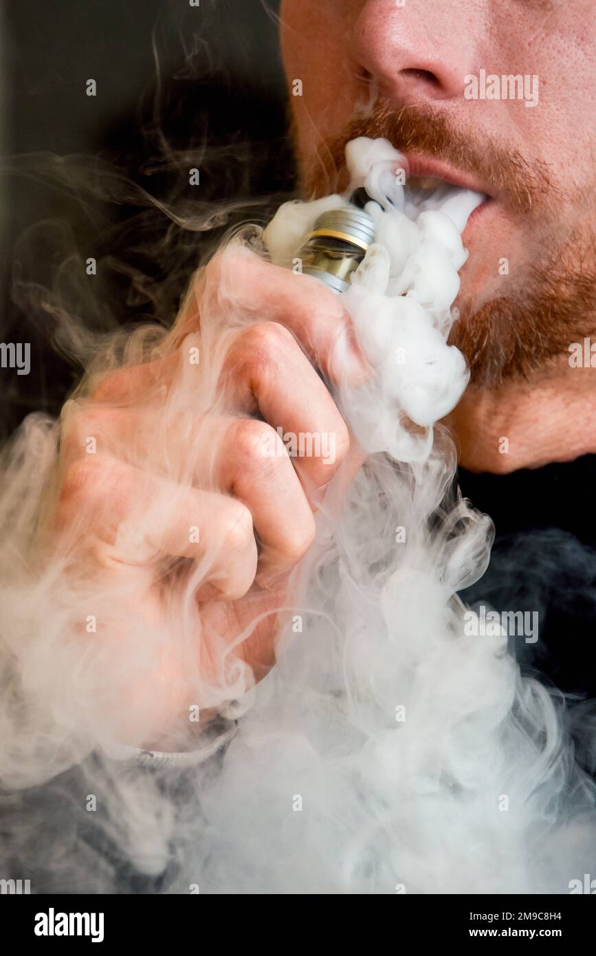 Close up of man smoking a vape device breathing out vape cloud Stock Photo