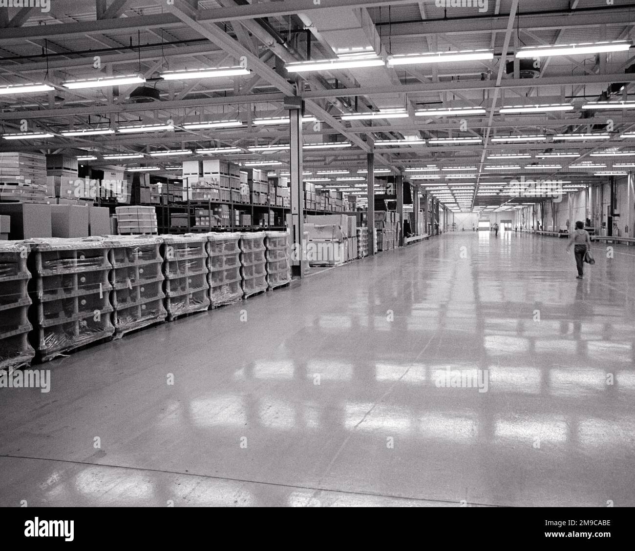 1970s SINGLE ANONYMOUS MAN WALKING IN VAST INTERIOR OF PARTS WAREHOUSE AT AUTOMOTIVE FACTORY WIDE OPEN CORRIDOR - i6330 HAR001 HARS INFRASTRUCTURE ANONYMOUS EMPLOYEE VAST BACK VIEW BLACK AND WHITE HAR001 LABORING OLD FASHIONED PARTS Stock Photo
