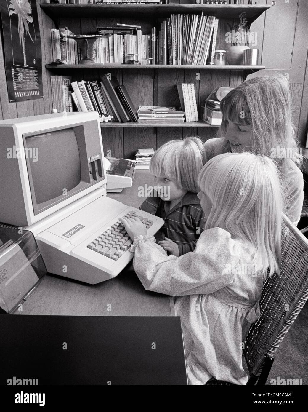 1980s MOTHER AND TWO CHILDREN USING HOME COMPUTER AT WORK STATION  - j14914 HAR001 HARS NOSTALGIA BROTHER OLD FASHION SISTER 1 JUVENILE COMMUNICATION BLOND YOUNG ADULT KEYBOARD TECHNOLOGY INFORMATION MYSTERY FAMILIES LIFESTYLE FEMALES BROTHERS HOME LIFE COPY SPACE LADIES COMPUTERS DAUGHTERS PERSONS MALES SIBLINGS SISTERS B&W HEAD AND SHOULDERS HIGH ANGLE DISCOVERY AND EXCITEMENT KNOWLEDGE PROGRESS INNOVATION OPPORTUNITY OCCUPATIONS SIBLING USING CONNECTION MONITOR HOME OFFICE COOPERATION JUVENILES MOMS TOGETHERNESS YOUNG ADULT WOMAN BLACK AND WHITE CAUCASIAN ETHNICITY COMPUTING HAR001 Stock Photo