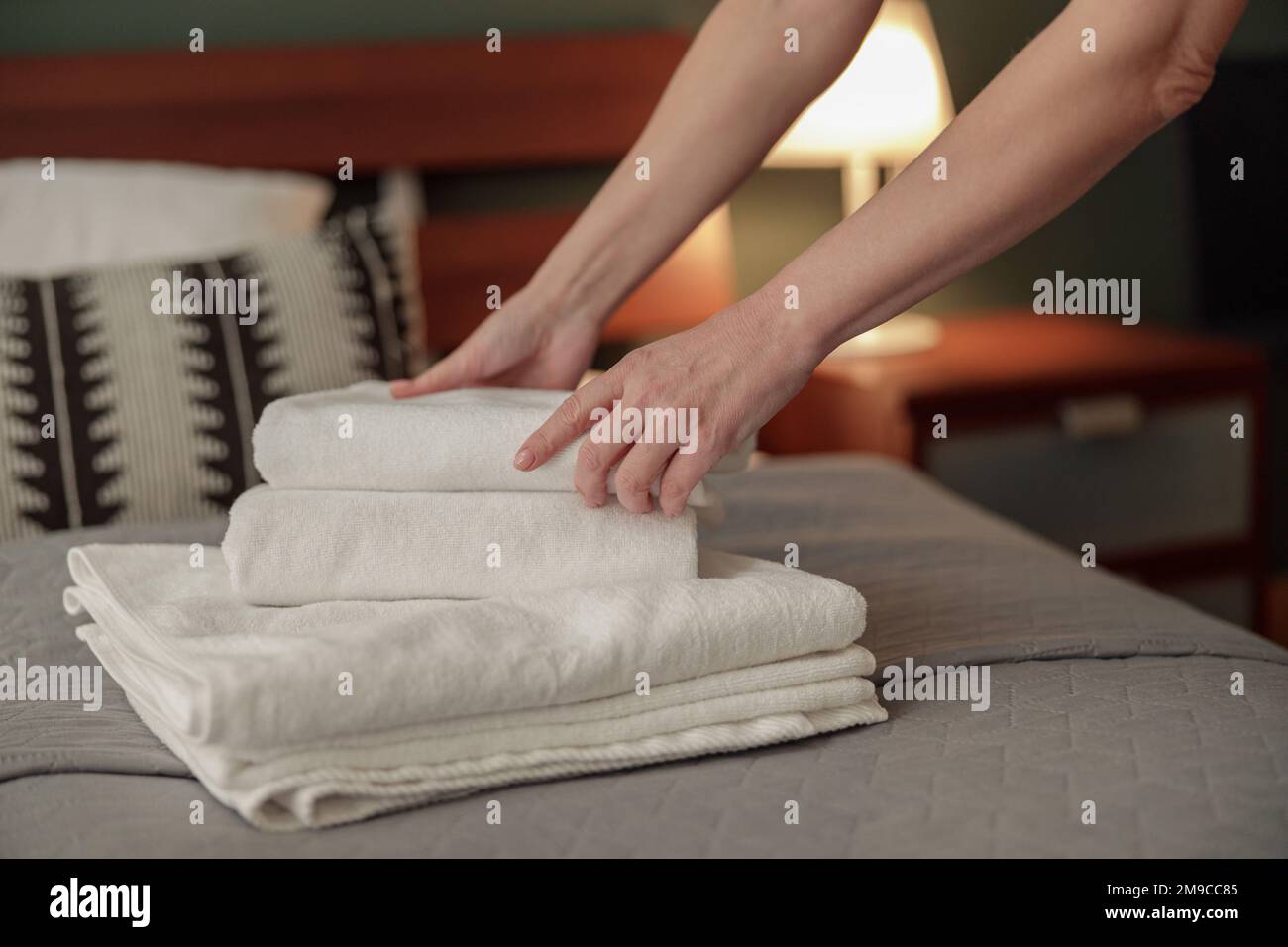 Closeup of maid hands putting stack of fresh white bath towels on bed