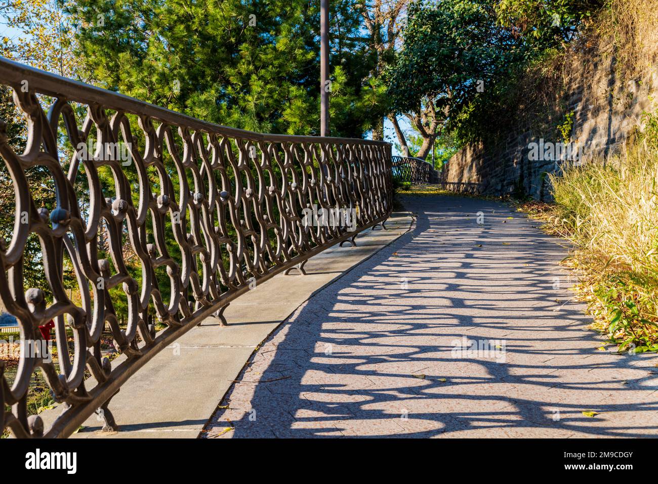 Sun casts long shadows on empty fenced path along Fairmount Water Works; Philadelphia; Pennsylvania; USA Stock Photo
