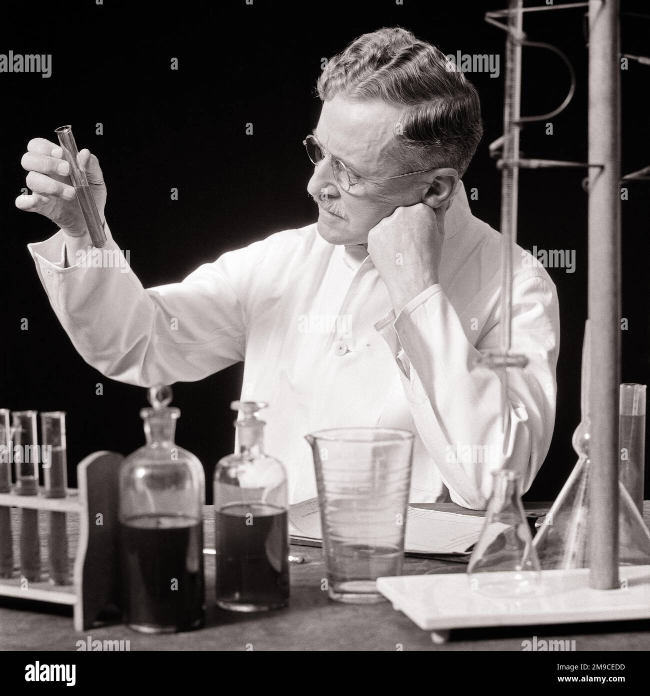 1930s MAN RESEARCH CHEMIST IN WHITE LAB COAT WEARING GLASSES WORKING EXAMINING TEST RESULTS THINKING PONDERING IN HIS LABORATORY - l1246 HAR001 HARS MALES MIDDLE-AGED B&W MIDDLE-AGED MAN GOALS HEALTHCARE VISION DREAMS PREVENTION DISCOVERY HIS HEALING CHEMIST SCIENTIFIC DIAGNOSIS BEAKER EXAMINING LEADERSHIP INNOVATION HEALTH CARE OCCUPATIONS TREATMENT RESULTS PONDERING CONCEPTUAL SINCERE SOLEMN CREATIVITY FOCUSED INTENSE SOLUTIONS TEST TUBES BLACK AND WHITE CAREFUL CAUCASIAN ETHNICITY DISEASE EARNEST HAR001 INTENT LABORATORIES LABS OLD FASHIONED Stock Photo