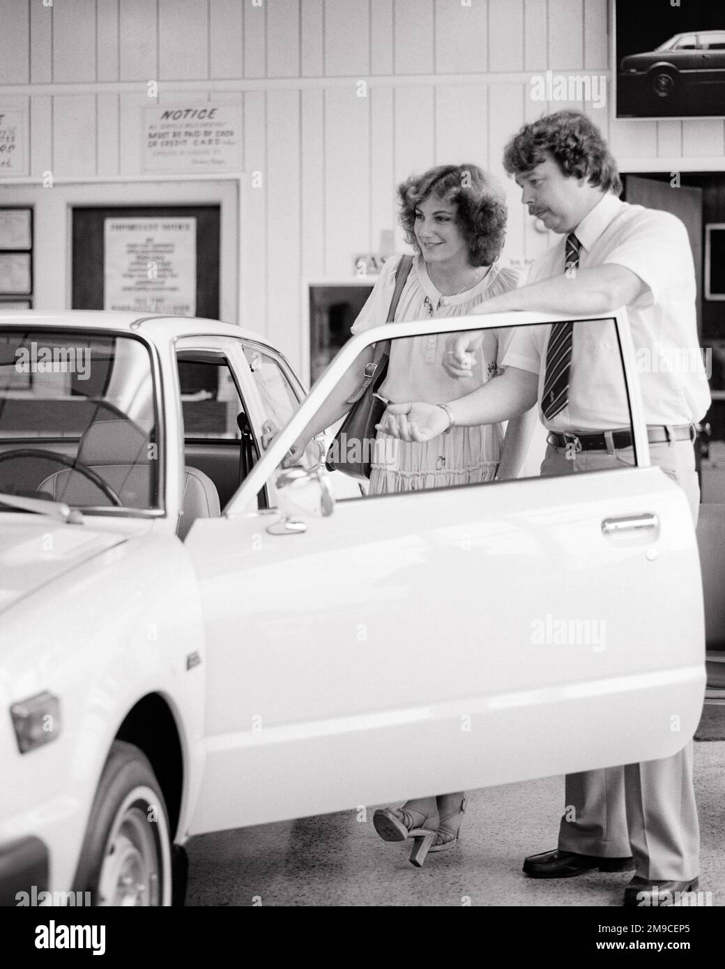 1970s CAR SALESMAN SHOWING A WOMAN CUSTOMER THE INTERIOR OF SEDAN IN THE DEALER SHOWROOM SALES OFFICE - m10239 HAR001 HARS JOBS SHOWING COPY SPACE HALF-LENGTH LADIES DEALERSHIP PERSONS BUY AUTOMOBILE MALES DEALER TRANSPORTATION B&W SHOPPER SHOPPERS SKILL DREAMS OCCUPATION SELLING SKILLS ADVENTURE CUSTOMER SERVICE SEDAN AUTOS OPPORTUNITY OCCUPATIONS PURCHASE AUTOMOBILES VEHICLES MID-ADULT MID-ADULT MAN SALESMEN YOUNG ADULT WOMAN BLACK AND WHITE CAUCASIAN ETHNICITY HAR001 OLD FASHIONED Stock Photo