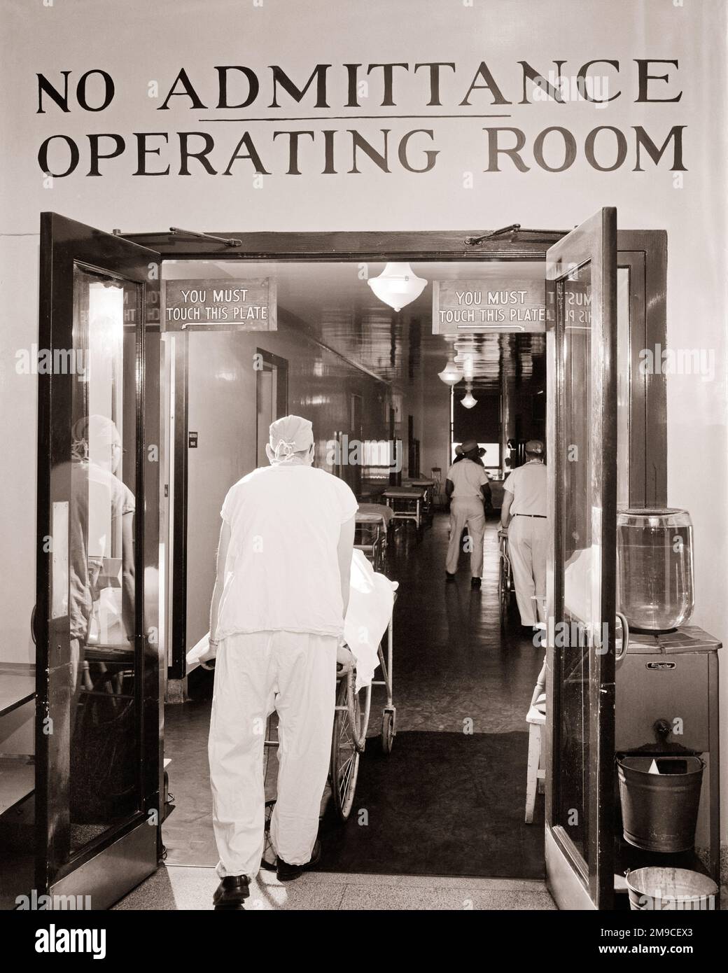 1950s BACK VIEW OF ORDERLY WEARING SCRUBS PUSHING GURNEY WITH PATIENT INTO THE OPERATING ROOM CORRIDOR SIGN SAYS NO ADMITTANCE - m1331 HAR001 HARS OCCUPATION OPERATING PREVENTION PROVIDER PROVIDERS PRACTITIONERS HEALING DIAGNOSIS GURNEY LOW ANGLE PHYSICIANS HEALTH CARE IMPAIRMENT OCCUPATIONS TREATMENT CORRIDOR HEALER HOSPITALS OPERATION ORDERLY PHYSICIAN PRACTITIONER SCRUBS FACILITY FACILITIES PROFESSIONALS SAYS BLACK AND WHITE CAUCASIAN ETHNICITY DISEASE HAR001 OLD FASHIONED Stock Photo
