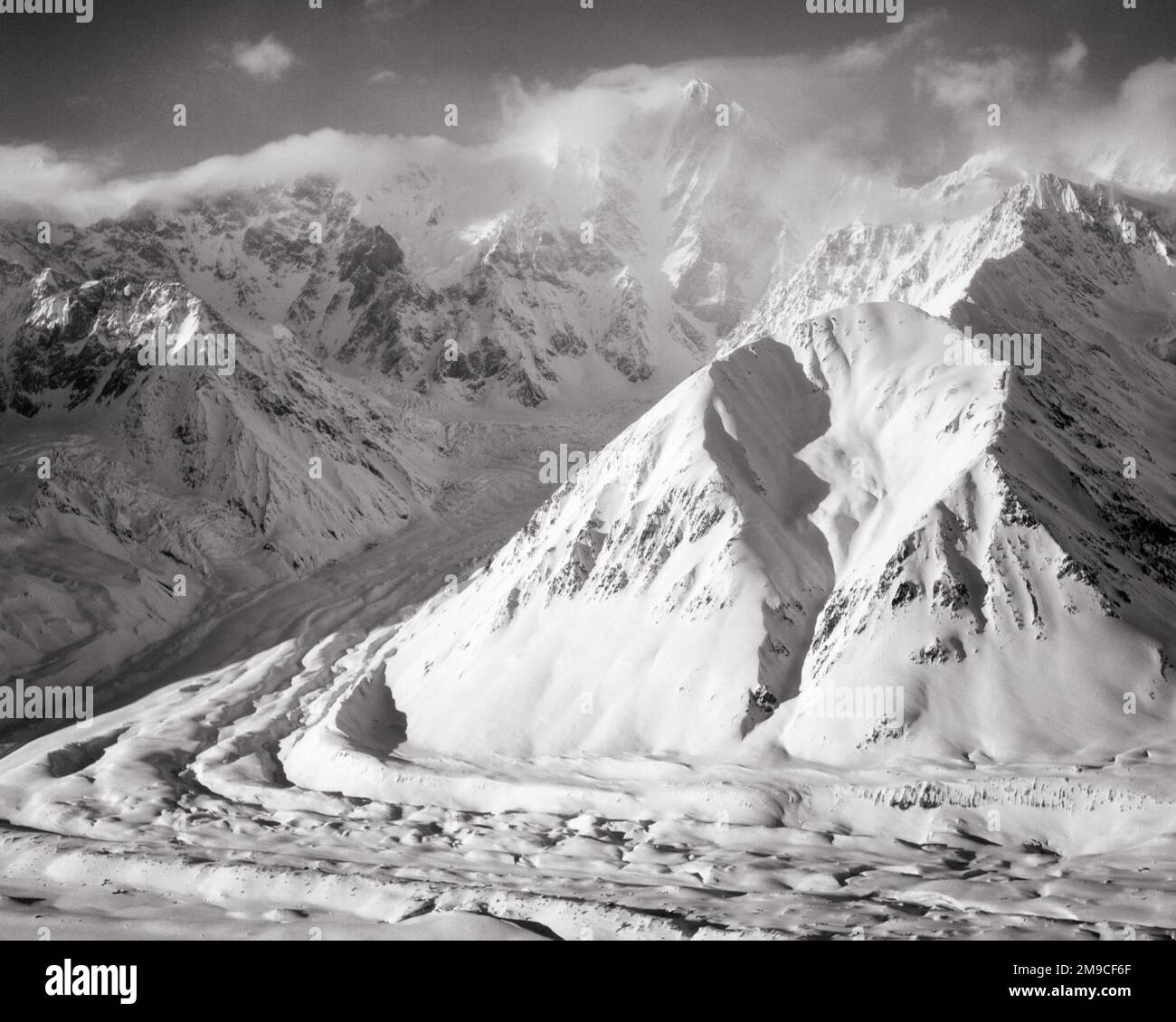 1950s LOOKING NORTH ON BLACK RAPIDS GLACIER WITH MOUNT HESS IN CENTER BACKGROUND WITH CLOUDS THE ALASKA RANGE ALASKA USA - m2658 HAR001 HARS RAPIDS RAPID WINTERY REMOTE 1937 AK BLACK AND WHITE HAR001 OLD FASHIONED RATE Stock Photo
