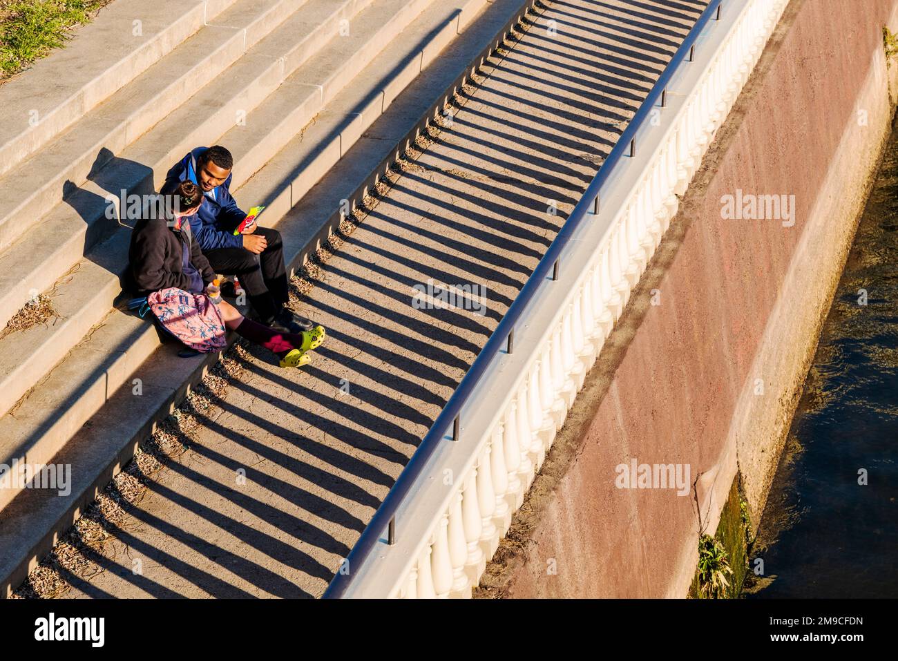 Multi-racial couple relax along sunlit stone path; Fairmount Water Works; Schuylkill River; Philadelphia; Pennsylvania; USA Stock Photo