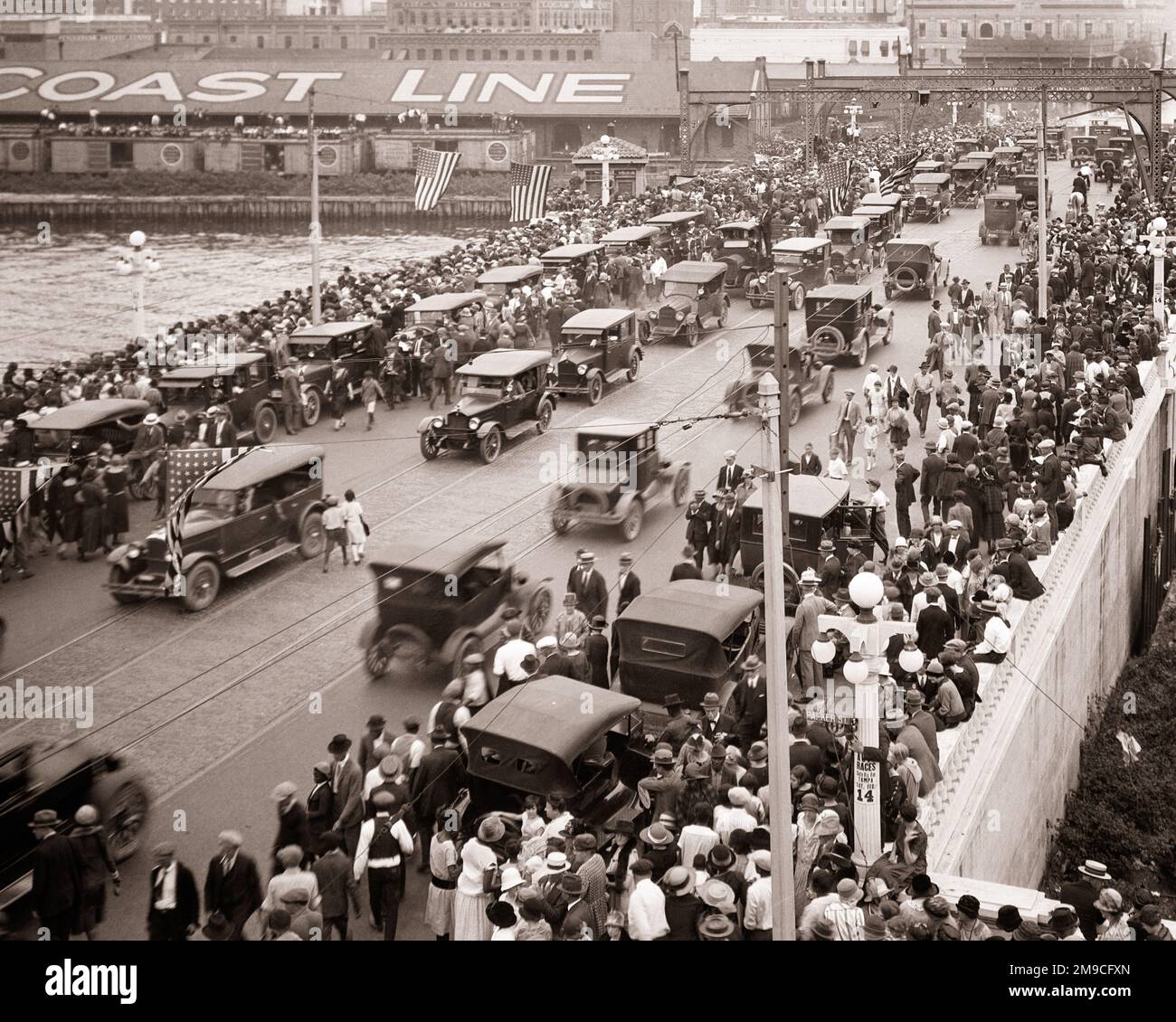 1920s LARGE DIVERSE CROWD OF PEDESTRIANS ON CROWDED SIDEWALKS AND ROAD OF A BRIDGE CARS PARKED AND ALSO MOVING TRAFFIC - m6786 CPC001 HARS BUSY NOSTALGIA MOVING OLD FASHION AUTO JUVENILE DIVERSE VEHICLE FLAGS RAILROAD JOY CELEBRATION CROWDS FEMALES ASSEMBLY LADIES MASS PERSONS AUTOMOBILE CUTOUT MALES PEDESTRIANS TRANSPORTATION SPECTATORS B&W GATHERING PARKED RAIL HIGH ANGLE AFRICAN-AMERICANS AFRICAN-AMERICAN AND AUTOS EXCITEMENT BLACK ETHNICITY CONNECTION SIDEWALKS AUTOMOBILES STARS AND STRIPES VARIOUS VEHICLES RAILROADS OLD GLORY VARIED COOPERATION HOLDAY RED WHITE AND BLUE SPAN THRONG Stock Photo