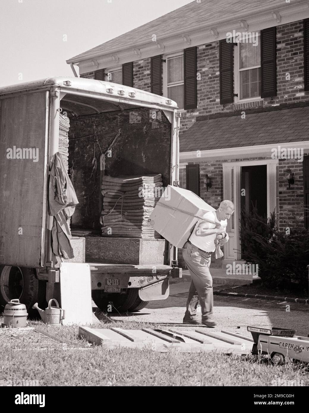 1960s ONE MAN UNLOADING MOVING VAN CARRYING LARGE BOX ON HIS BACK USING