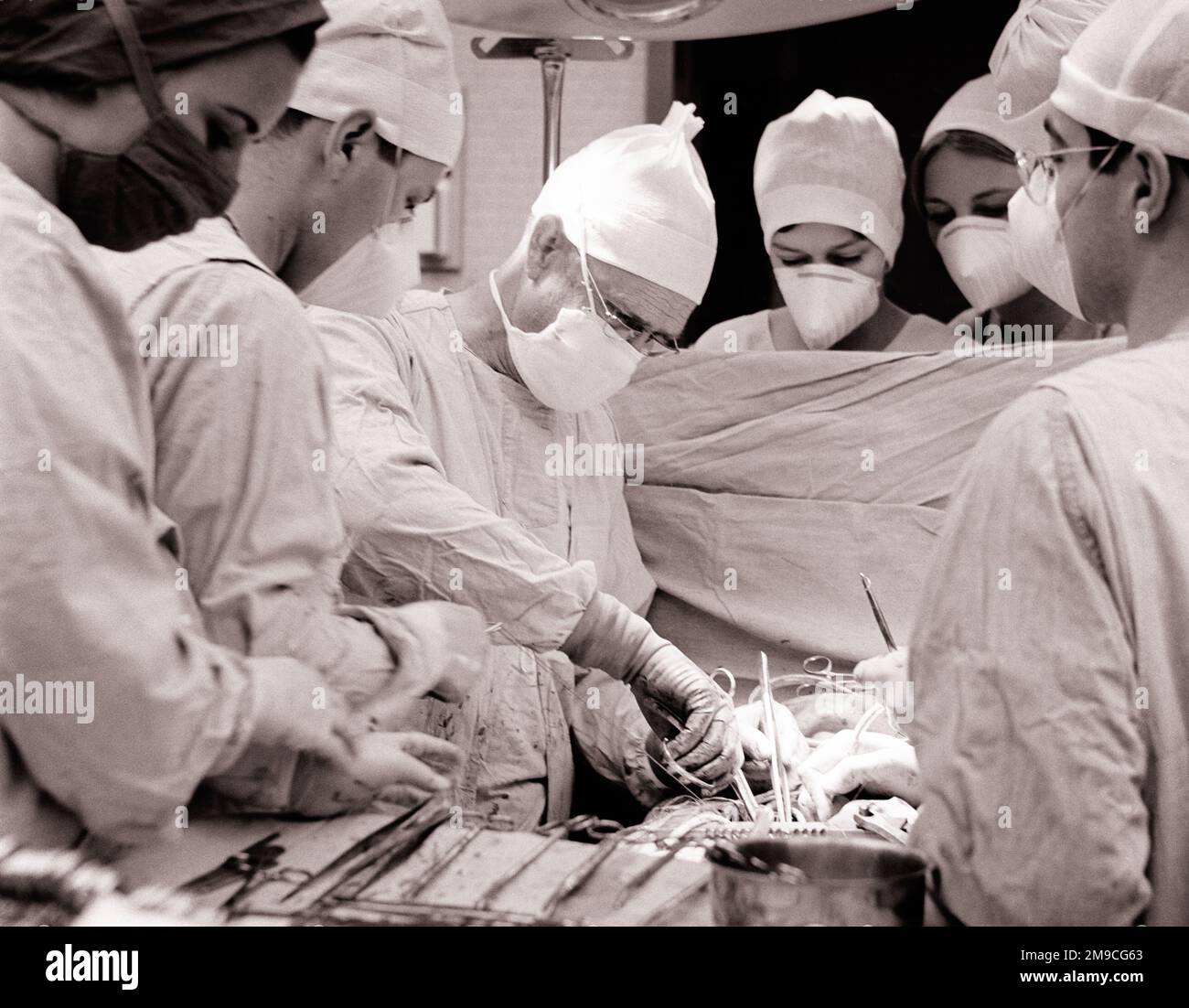 1960s SURGEON WITH ASSISTING DOCTORS AND NURSES PERFORMING OPEN HEART SURGERY - m7837 HAR001 HARS INSPIRATION MALES SIX PROFESSION CONFIDENCE MIDDLE-AGED B&W MIDDLE-AGED MAN HEALTHCARE PERFORMING SURGERY SKILL OCCUPATION SKILLS OPERATING PREVENTION PROVIDER PROVIDERS PRACTITIONERS HEALING AND DIAGNOSIS SURGICAL CAREERS EXCITEMENT LEADERSHIP PHYSICIANS PROGRESS INNOVATION LABOR OPERATING ROOM HEALTH CARE EMPLOYMENT IMPAIRMENT OCCUPATIONS SURGEON TREATMENT CONNECTION HEALER CONCEPTUAL HOSPITALS OPERATION PHYSICIAN PRACTITIONER SUPPORT FACILITY INFRASTRUCTURE EMPLOYEE FACILITIES ASSISTING Stock Photo