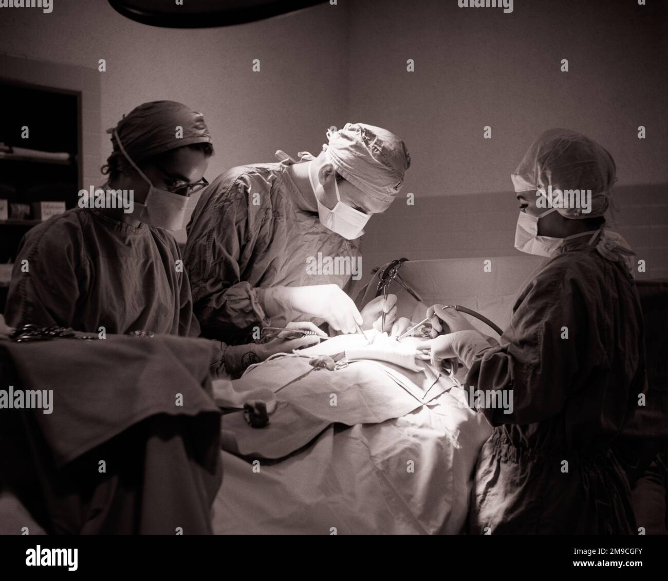 1960s MAN DOCTOR SURGEON AND TWO WOMEN ATTENDANT SURGICAL NURSES ASSISTING PERFORMING A SURGERY IN HOSPITAL OPERATING ROOM - m8986 HAR001 HARS TEAMWORK FEMALES JOBS ILLNESS COPY SPACE HALF-LENGTH LADIES PERSONS CARING MALES RISK PROFESSION CONFIDENCE B&W GOALS HEALTHCARE PERFORMING SURGERY SKILL OCCUPATION SKILLS OPERATING PREVENTION PROVIDER PROVIDERS PRACTITIONERS HEALING AND DIAGNOSIS SURGICAL CAREERS KNOWLEDGE LEADERSHIP LOW ANGLE PHYSICIANS LABOR OPERATING ROOM HEALTH CARE EMPLOYMENT IMPAIRMENT OCCUPATIONS SURGEON TREATMENT CONNECTION HEALER HOSPITALS OPERATION PHYSICIAN PRACTITIONER Stock Photo