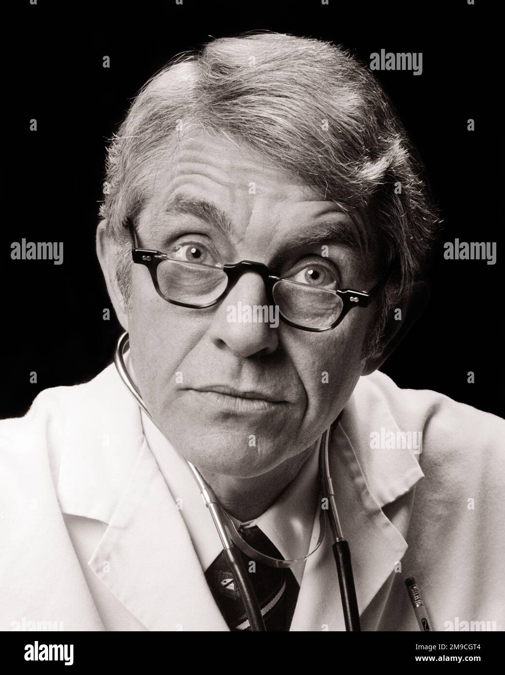 1970s PORTRAIT OF DOCTOR WITH SURPRISED FACIAL EXPRESSION WEARING HALF-LENS READING EYEGLASSES LOOKING AT CAMERA - m9870 HAR001 HARS FEAR CAREER SHOCK SHOCKED COMIC JOBS STUDIO SHOT ILLNESS COPY SPACE PERSONS THOUGHTFUL CARING CHARACTER MALES PROFESSION EYEGLASSES EXPRESSIONS AMAZED MIDDLE-AGED B&W WIDE LENS MIDDLE-AGED MAN EYE CONTACT HEALTHCARE SKILL BUG-EYED AWE HUMOROUS OCCUPATION SKILLS PREVENTION HEAD AND SHOULDERS PROVIDER PROVIDERS PRACTITIONERS HEALING DIAGNOSIS CAREERS EXCITEMENT PHYSICIANS COMICAL HALF HEALTH CARE IMPAIRMENT OCCUPATIONS TREATMENT HEALER COMEDY PHYSICIAN PRACTITIONER Stock Photo