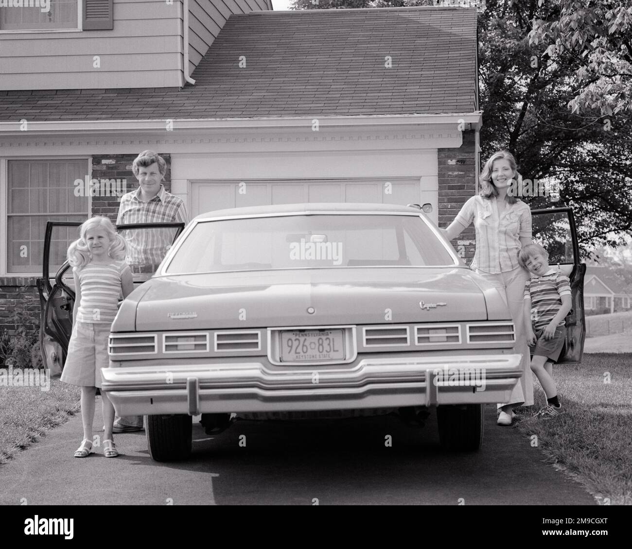 1970s HAPPY FAMILY OF FOUR POSED STANDING BY OPEN DOORS OF CAR IN DRIVEWAY OF THEIR SUBURBAN HOME MOTHER FATHER SON DAUGHTER - m9887 HAR001 HARS FOUR MOM NOSTALGIC PAIR 4 SUBURBAN DOORS MOTHERS OLD TIME NOSTALGIA OLD FASHION AUTO SISTER DRIVEWAY JUVENILE VEHICLE YOUNG ADULT TEAMWORK SONS PLEASED FAMILIES JOY LIFESTYLE SATISFACTION FEMALES HOUSES READY MARRIED SPOUSE HUSBANDS HEALTHINESS HOME LIFE COPY SPACE FRIENDSHIP FULL-LENGTH LADIES DAUGHTERS PERSONS INSPIRATION RESIDENTIAL AUTOMOBILE MALES BUILDINGS SISTERS TRANSPORTATION FATHERS B&W PARTNER SUMMERTIME EYE CONTACT HAPPINESS CHEERFUL Stock Photo