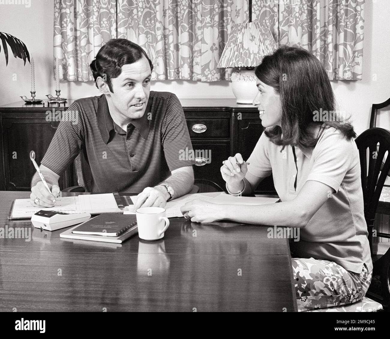 1970s COUPLE SITTING AT DINING ROOM TABLE GOING OVER BILLS SCHEDULES CALENDAR HOUSEHOLD BUDGET - s20347 HAR001 HARS 1 CALCULATOR HOUSEHOLD BUDGET STYLE COMMUNICATION YOUNG ADULT TEAMWORK INFORMATION LIFESTYLE SATISFACTION FEMALES MARRIED SPOUSE HUSBANDS HOME LIFE FINANCES COPY SPACE FRIENDSHIP HALF-LENGTH LADIES PERSONS MALES B&W PARTNER BRUNETTE HAPPINESS HIGH ANGLE CHECKBOOK CONNECTION MUG SUPPORT DINING ROOM CHECKS COOPERATION TOGETHERNESS WIVES YOUNG ADULT MAN BLACK AND WHITE CAUCASIAN ETHNICITY HAR001 OLD FASHIONED Stock Photo