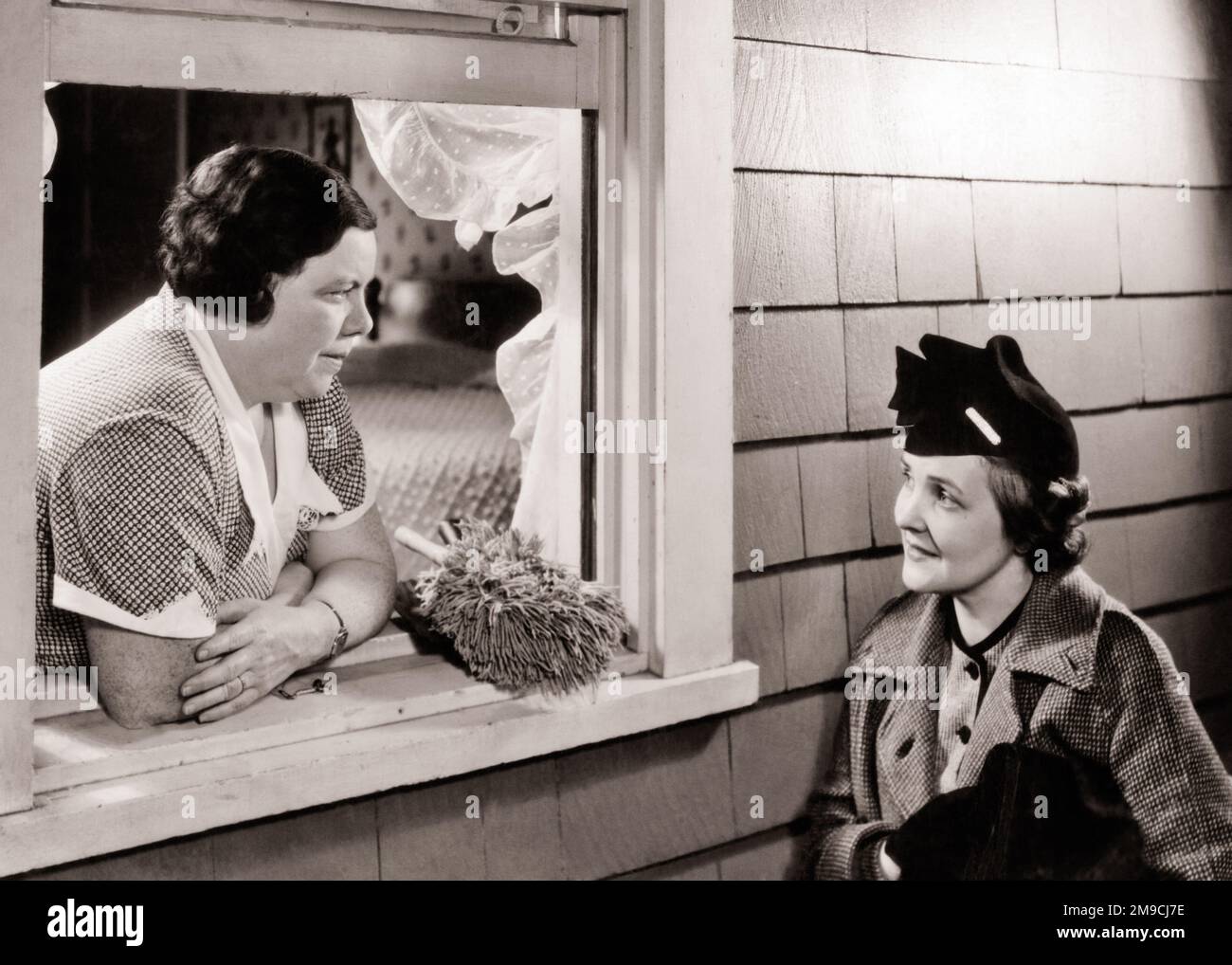 1930s TWO WOMEN GOSSIPING HOUSEWIFE LEANING OUT WINDOW WITH DUSTER TALKING TO WOMAN NEIGHBOR WEARING HAT COAT - s7904 HAR001 HARS FRIENDSHIP HALF-LENGTH LADIES MAID PERSONS SIBLINGS SISTERS DUSTER GOSSIPING MIDDLE-AGED B&W HOMEMAKER HOMEMAKERS MIDDLE-AGED WOMAN NEIGHBORHOOD HOUSEWIVES SIBLING NEIGHBOR RUMOR STYLISH OPEN WINDOW TOGETHERNESS WINDOW SILL BLACK AND WHITE CAUCASIAN ETHNICITY HAR001 OLD FASHIONED Stock Photo