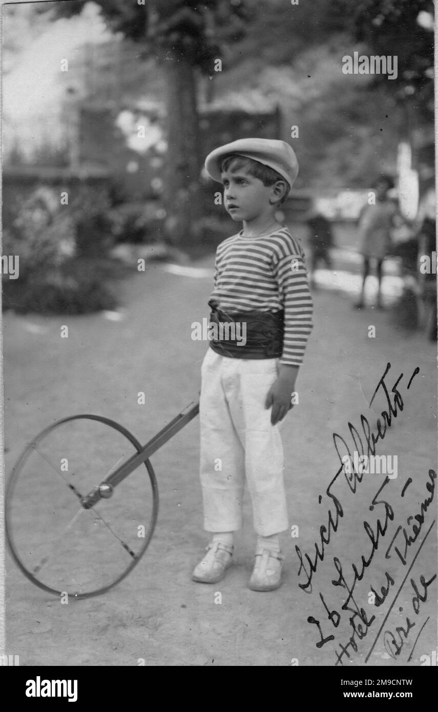 A little boy with a wheel marker, in Italy.  He is dressed in white trousers, a striped top and a large flat cap. Stock Photo