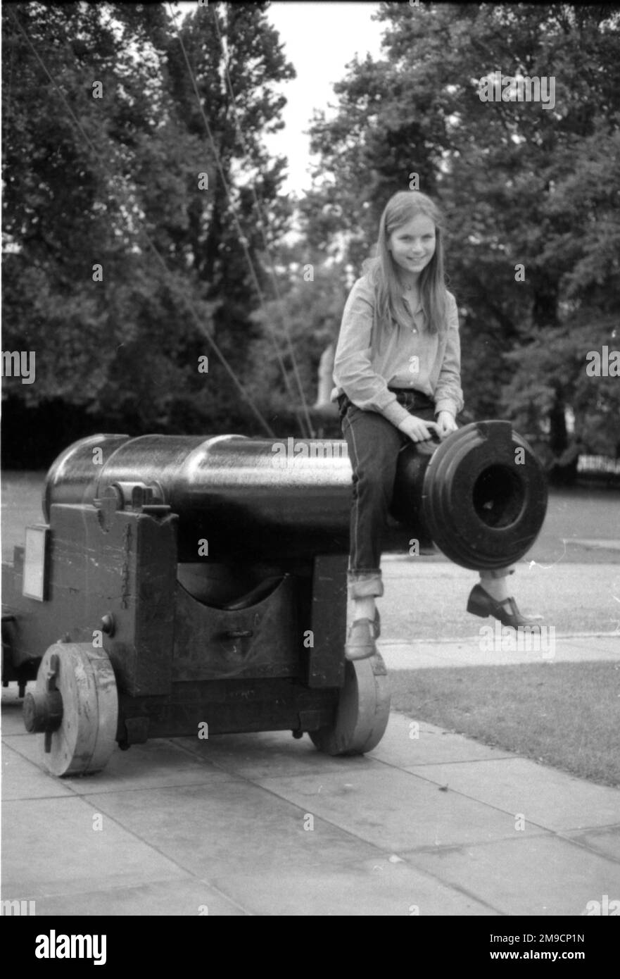 A little girl sits on a large cannon in Greenwich, south east London. Stock Photo